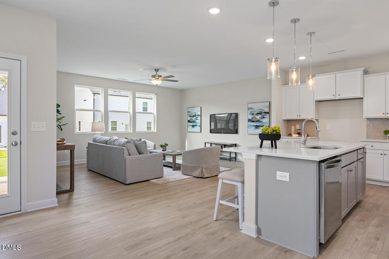 Open-concept living room with gray sofa and kitchen featuring white cabinets, gray island in Davidson Homes The Preston A, Lillington, NC
