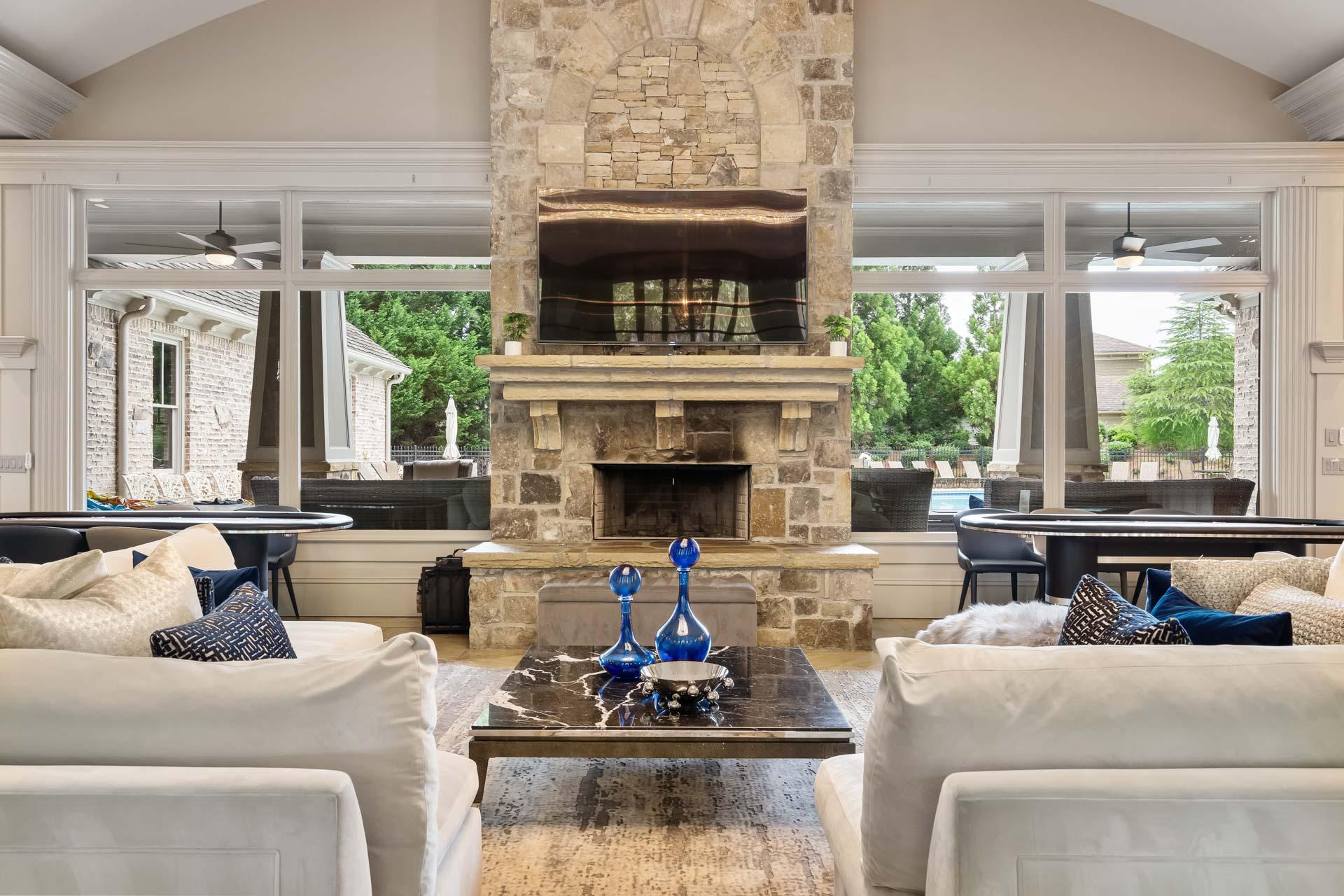 Luxurious great room with tall stone fireplace, white sofas, marble table, and pool view at The Village at Towne Lake in Woodstock GA