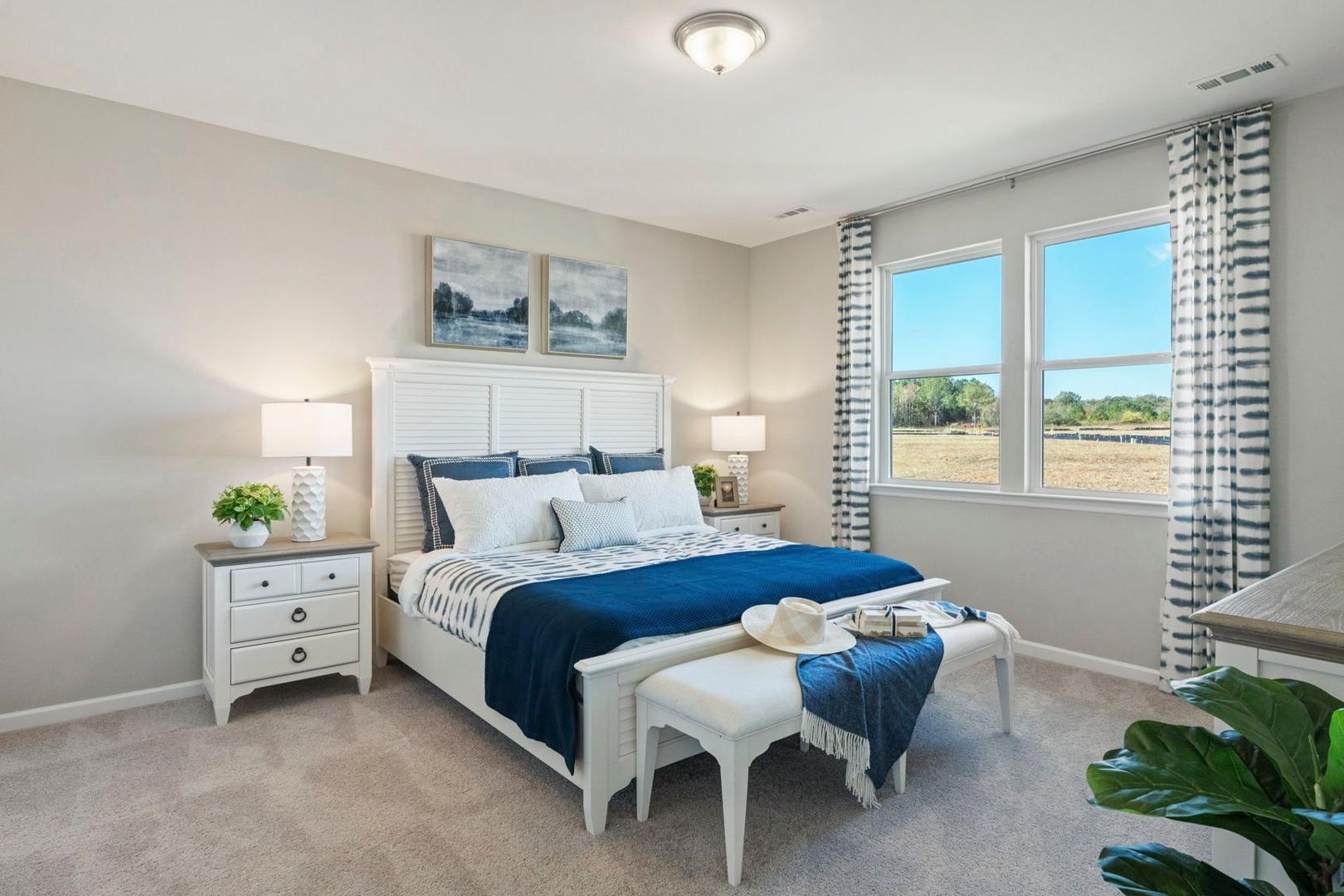 Spacious master bedroom in The Phoenix home with white king bed, blue bedding, large windows, and neutral decor