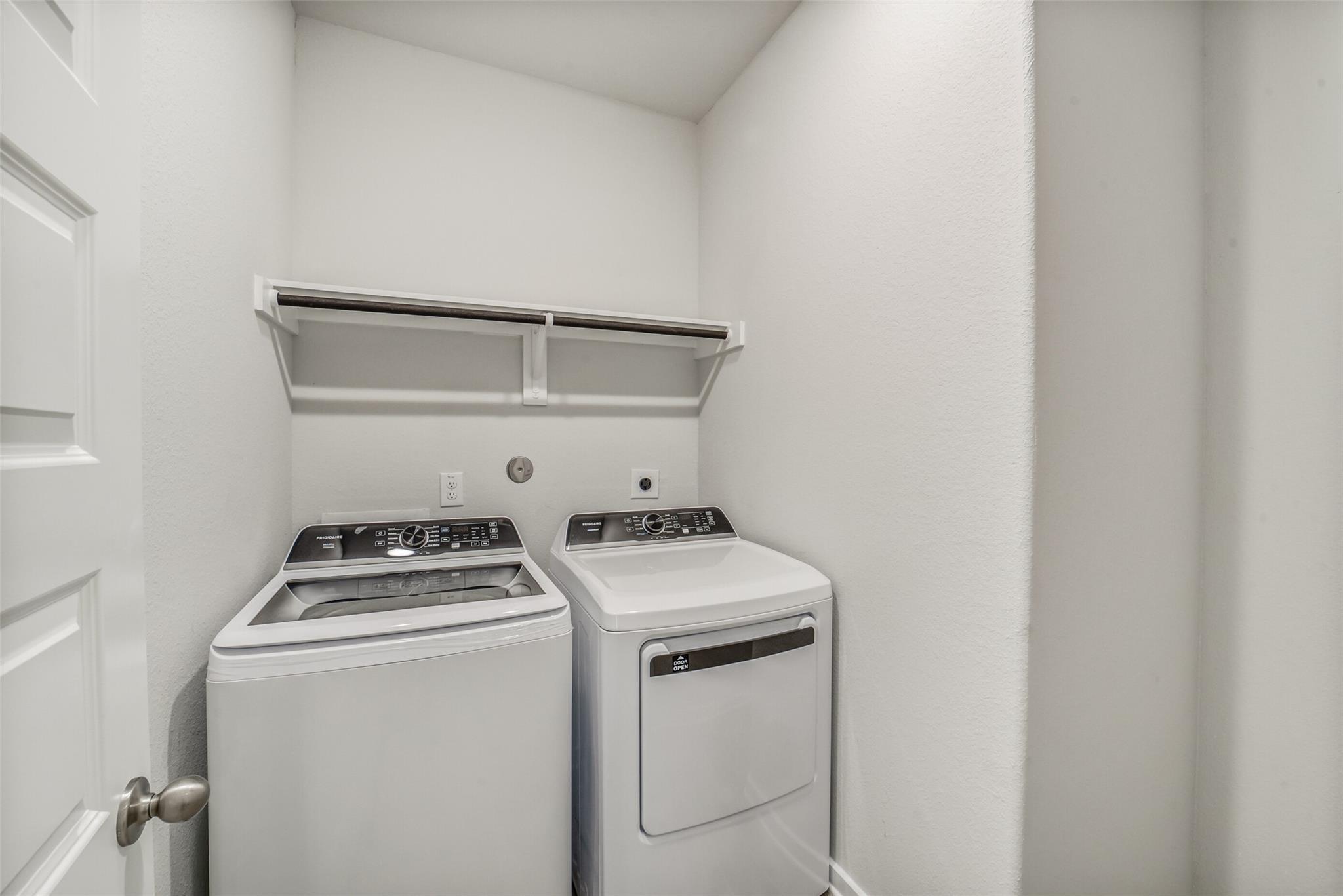 Bright laundry room with Frigidaire washer, dryer and folding shelf in 4-bedroom Acadia C home, Windmill Estates, Magnolia, Texas