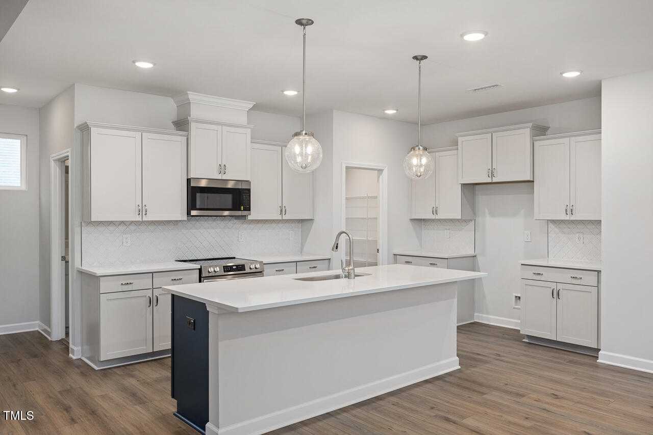 Modern white kitchen with quartz island, stainless appliances, subway tile backsplash in Davidson Homes The Adalynn B, Lillington, NC