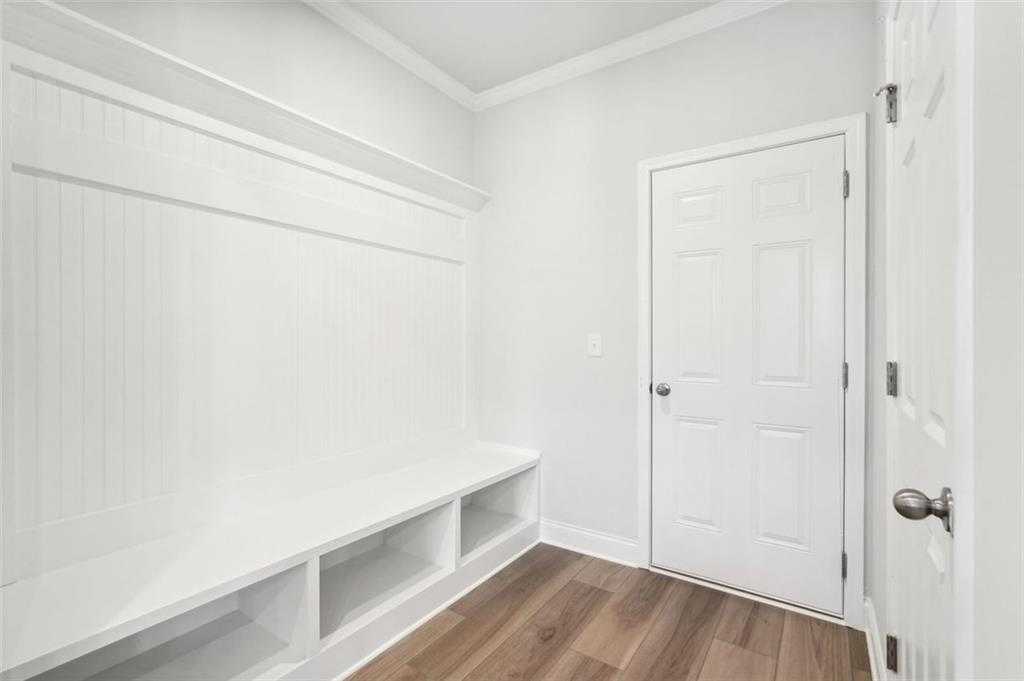 Bright mudroom with white shiplap built-ins, benches, cabinets, and hooks on hardwood floors in Davidson Homes The Hickory C, Hoschton, GA