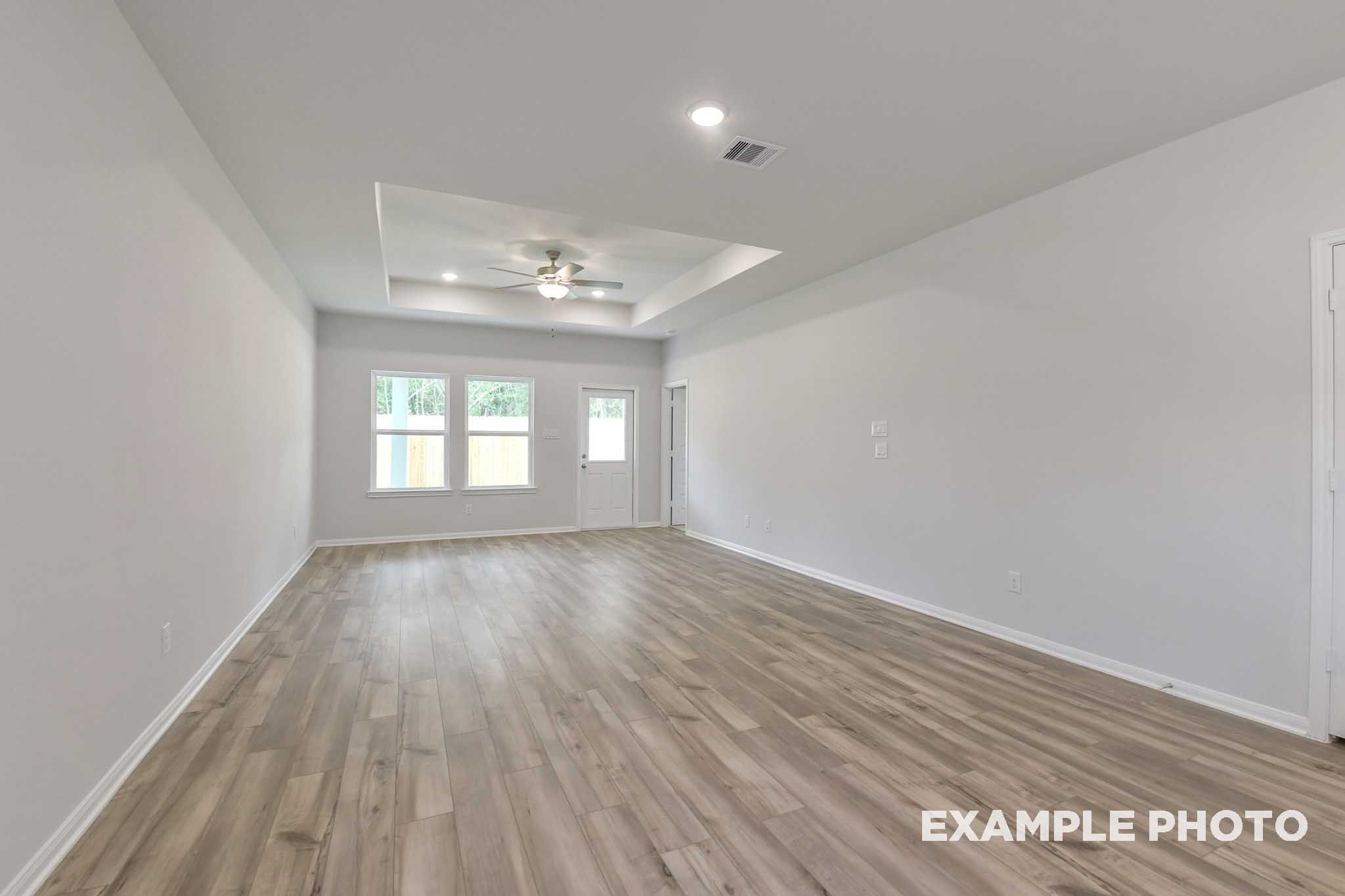 Spacious open-concept living area in The Frio floor plan featuring a tray ceiling and wood-style flooring in Conroe, Texas.