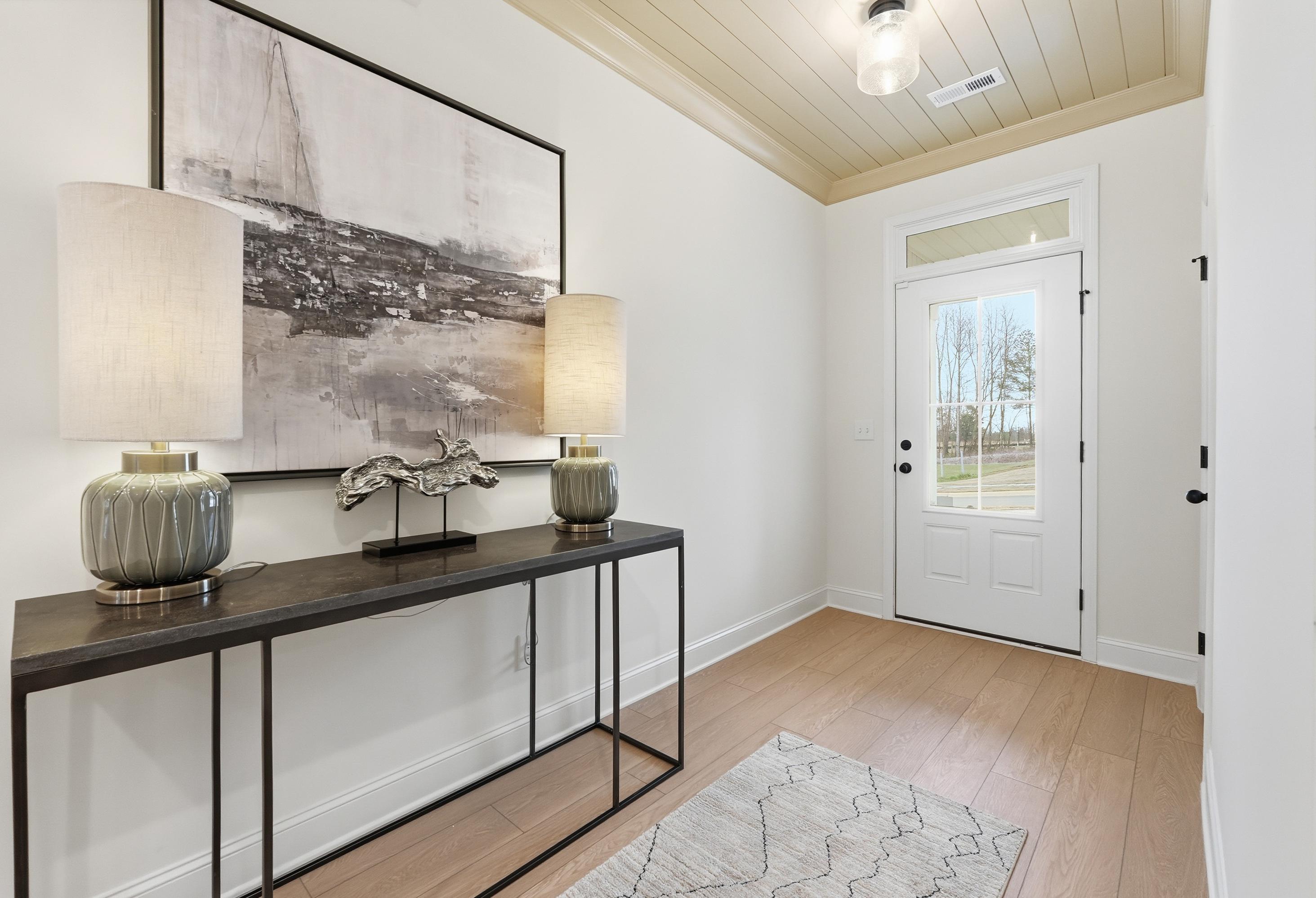 Modern entryway in The Laurel home featuring console table, nautical artwork, lamps, and white front door