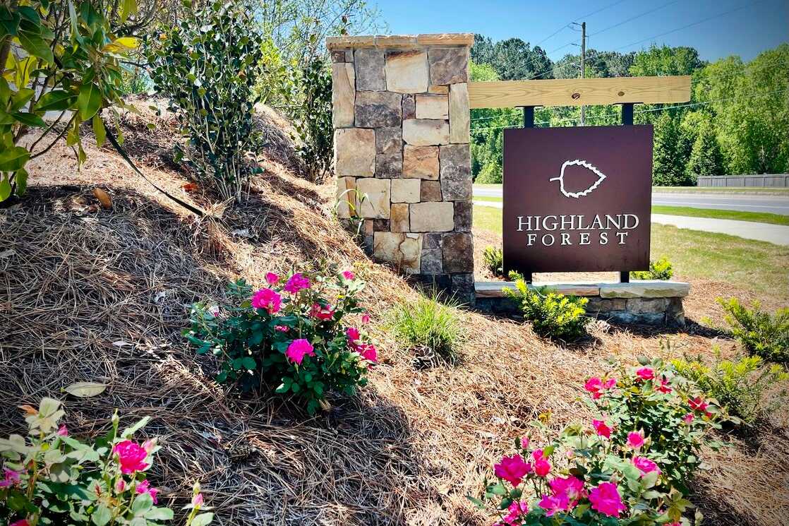 Highland Forest entrance sign in Fuquay-Varina NC with stone pillar, leaf emblem, pink azaleas and lush greenery