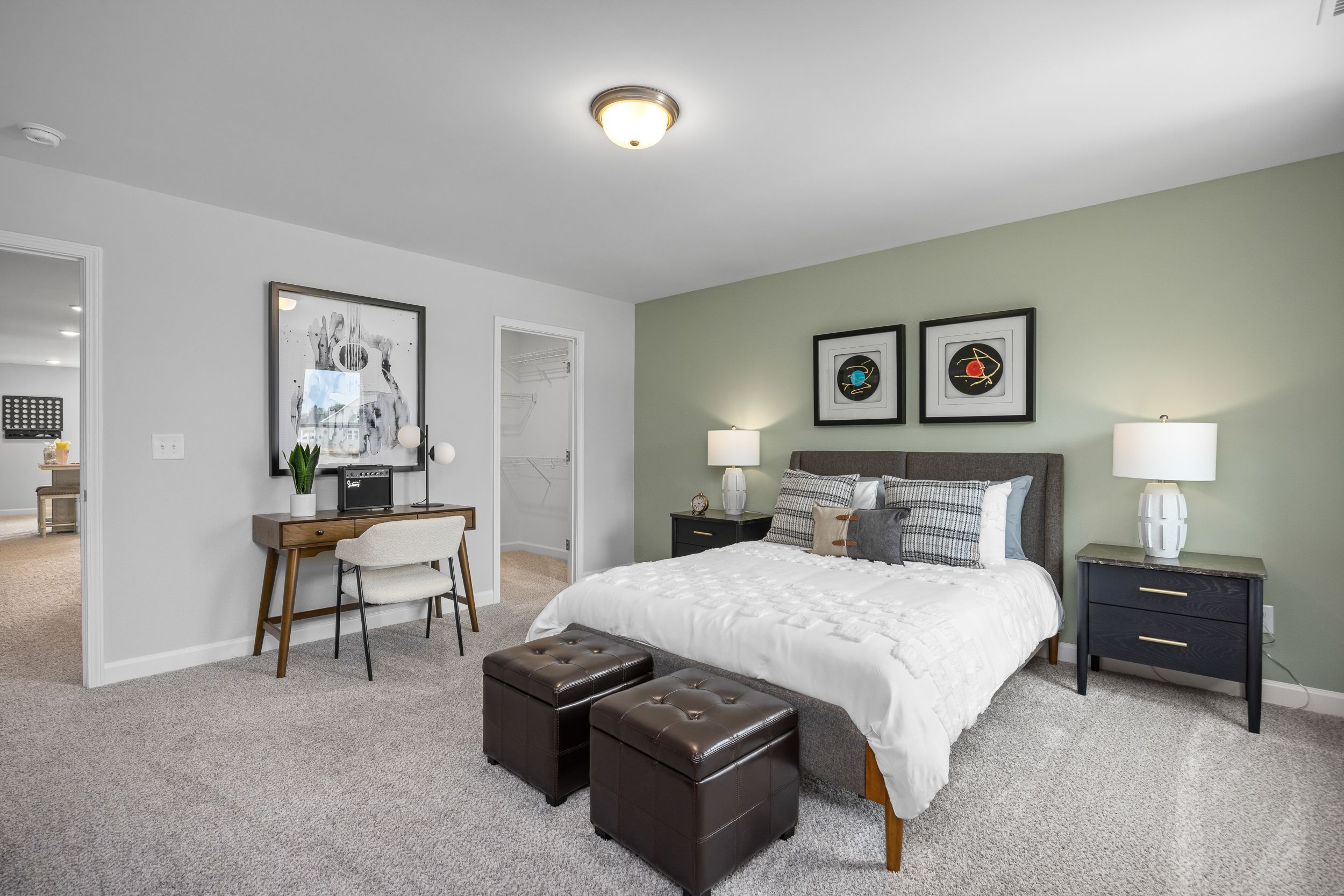 Spacious master bedroom in The Magnolia B with king bed, desk workspace, green accent wall, and modern decor