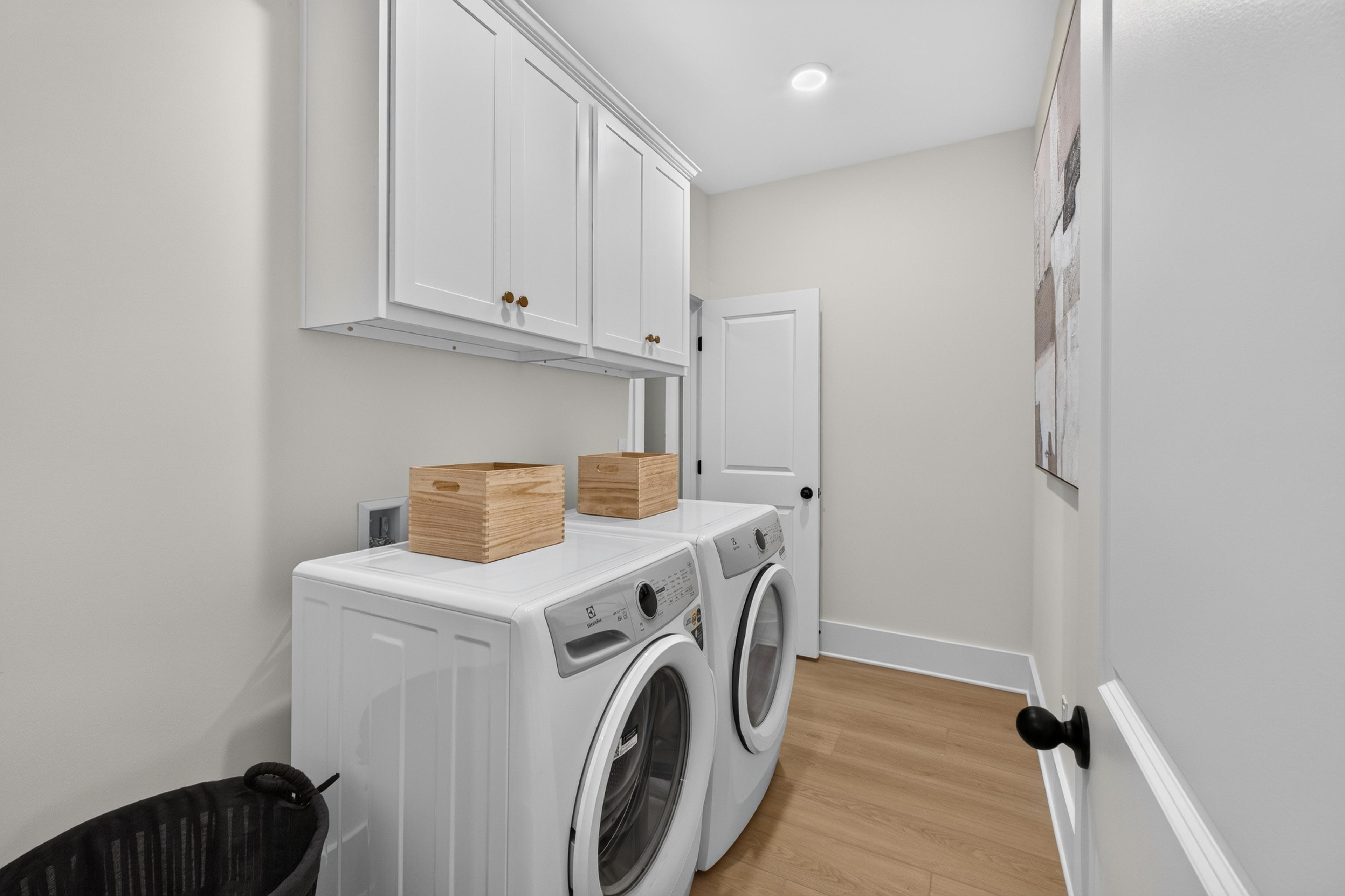 Laundry room with white washer and dryer, overhead cabinets, and hardwood floors at Evergreen Mill in Madison, Alabama