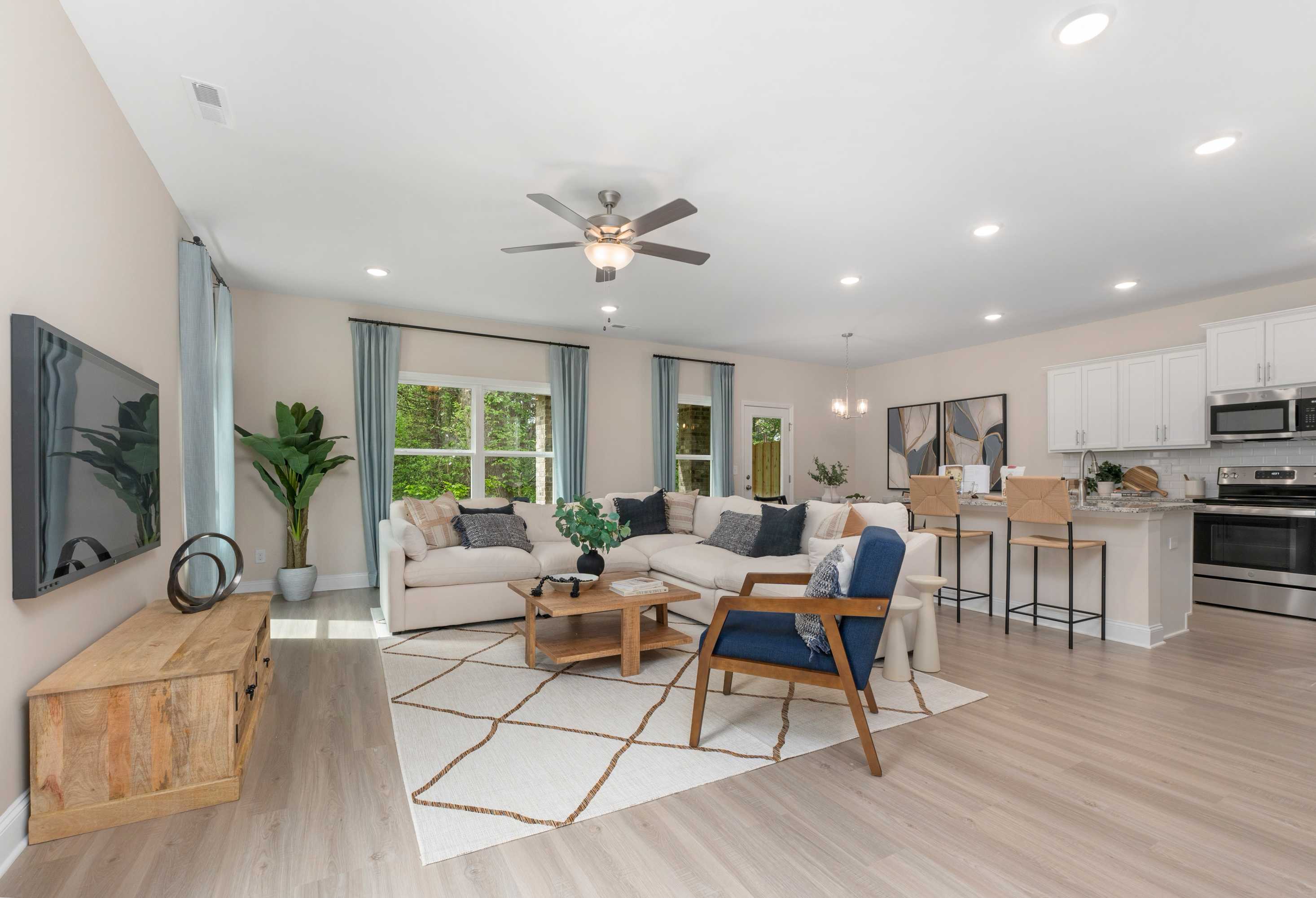 Spacious open-concept living room in The Camden B with beige L-shaped sofa, navy armchair, potted plants, and modern white kitchen by Davidson Homes