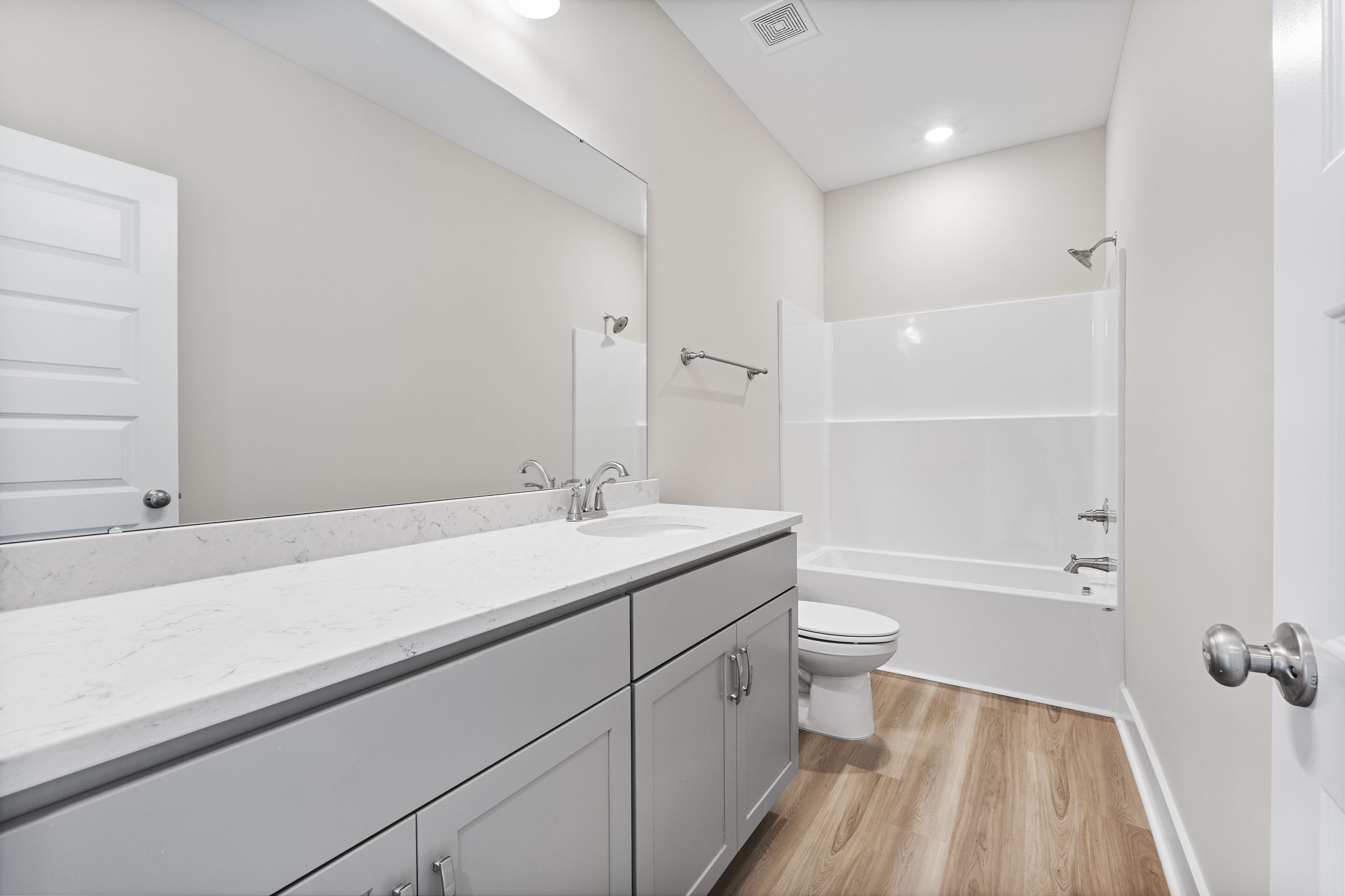 Master bathroom in The Oxford A with white subway tile shower-tub, gray double vanity, quartz countertop, and wood flooring