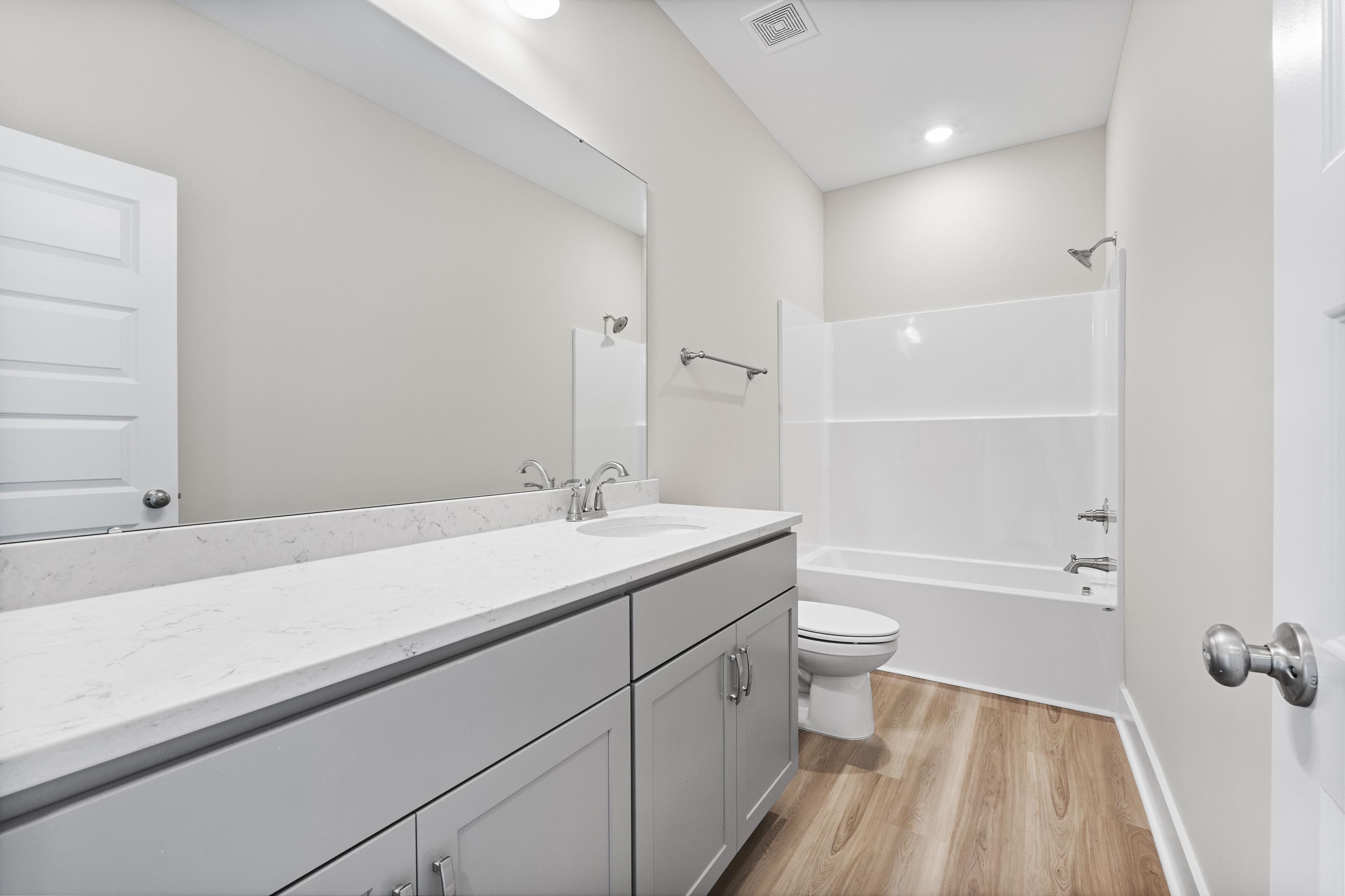Master bathroom in The Oxford A with white subway tile shower-tub, gray double vanity, quartz countertop, and wood flooring
