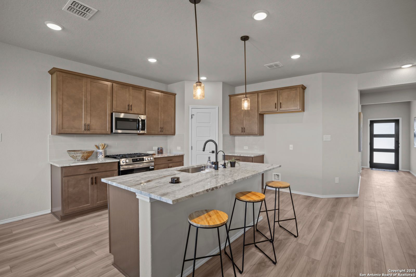 Modern kitchen with large white quartz island, beige shaker cabinets, stainless appliances in Davidson Homes The Asheville H, Converse TX