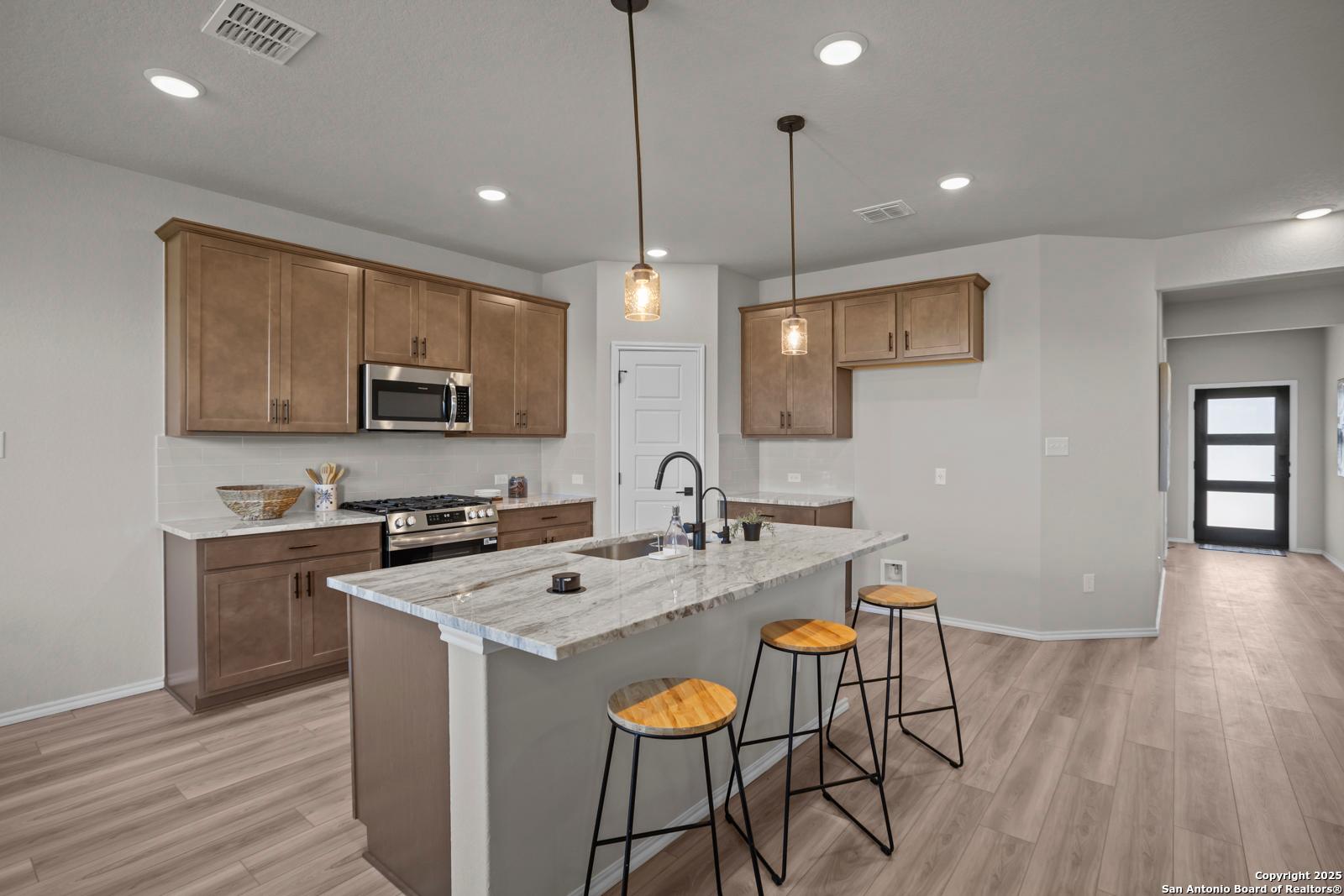 Modern kitchen with large white quartz island, beige shaker cabinets, stainless appliances in Davidson Homes The Asheville H, Converse TX