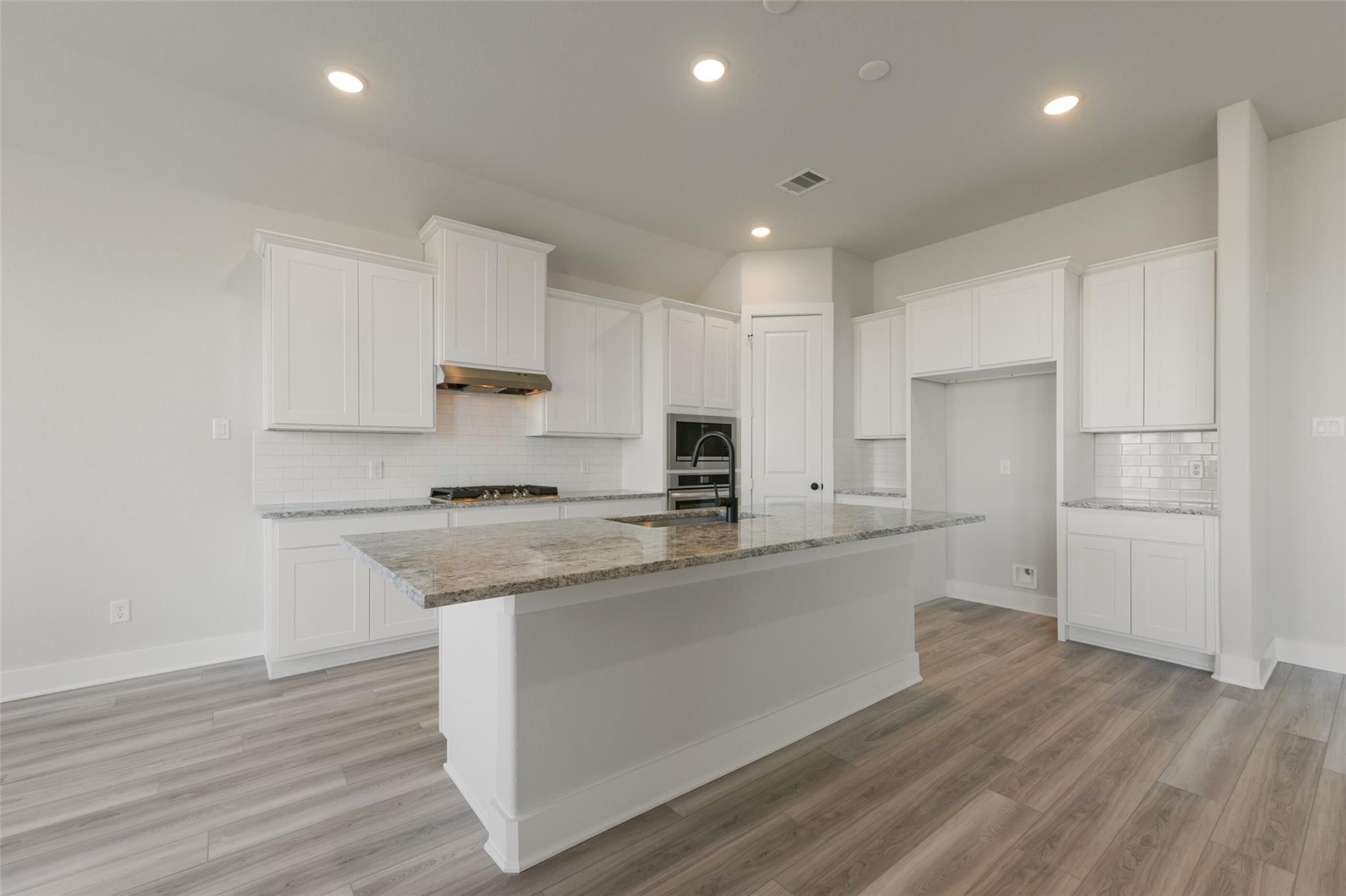Modern white kitchen featuring granite island, stainless appliances, and subway tile backsplash in Davidson Homes The Edward C, Texas City