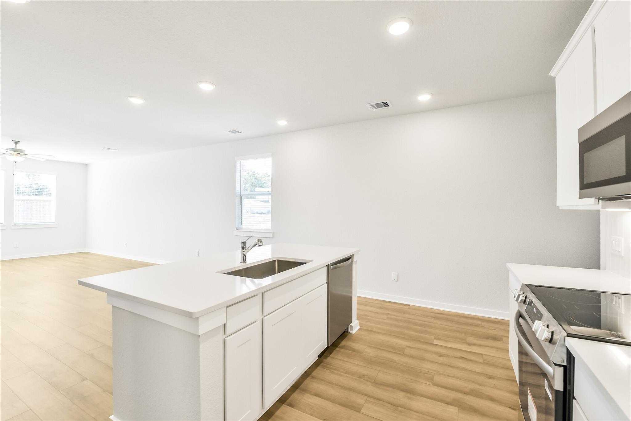 Modern white kitchen island with sink, dishwasher, and stainless appliances in open layout, San Marcos E by Davidson Homes, Cleveland TX