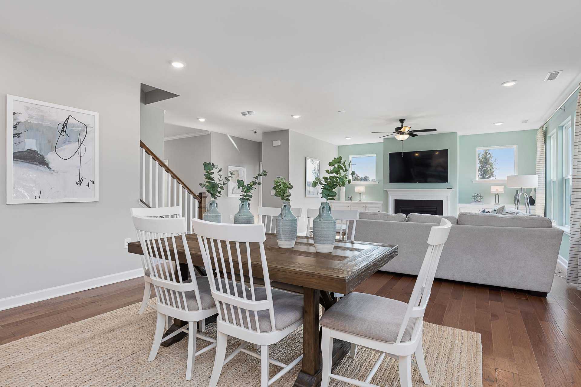 Open-concept dining and living room in Highland Forest, Fuquay-Varina NC with wooden table, white chairs, gray sofa, fireplace, and hardwood floors