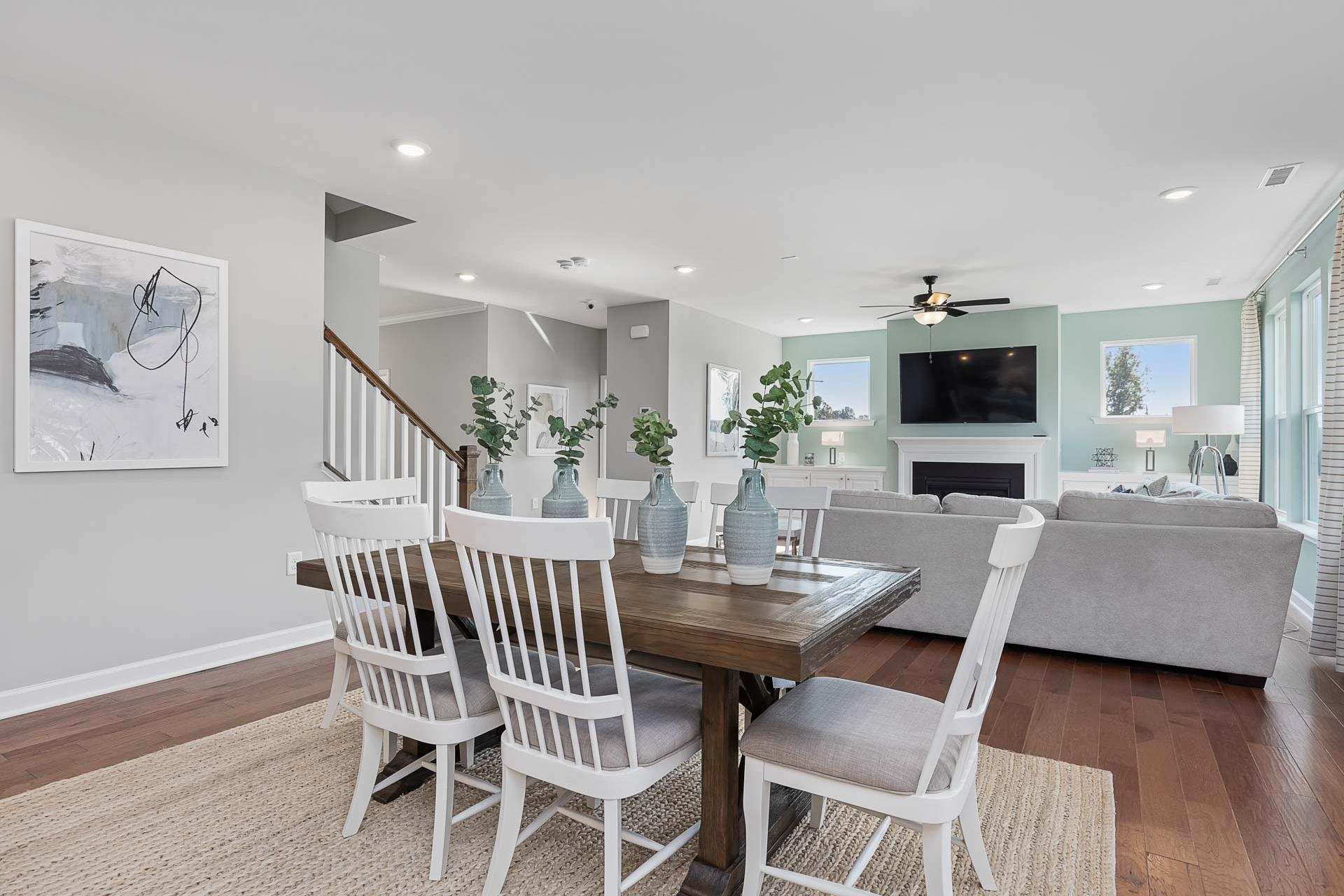 Open-concept dining and living room in Highland Forest, Fuquay-Varina NC with wooden table, white chairs, gray sofa, fireplace, and hardwood floors