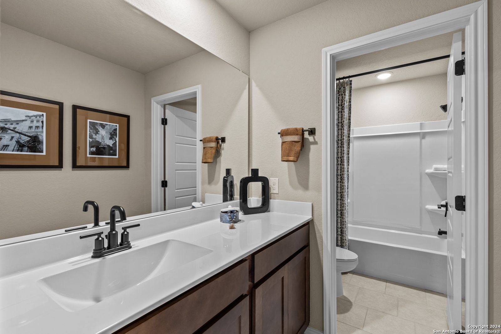 Elegant master bathroom with double vanity, tub-shower combo, and framed art in Davidson Homes The Douglas F, Bricewood, San Antonio