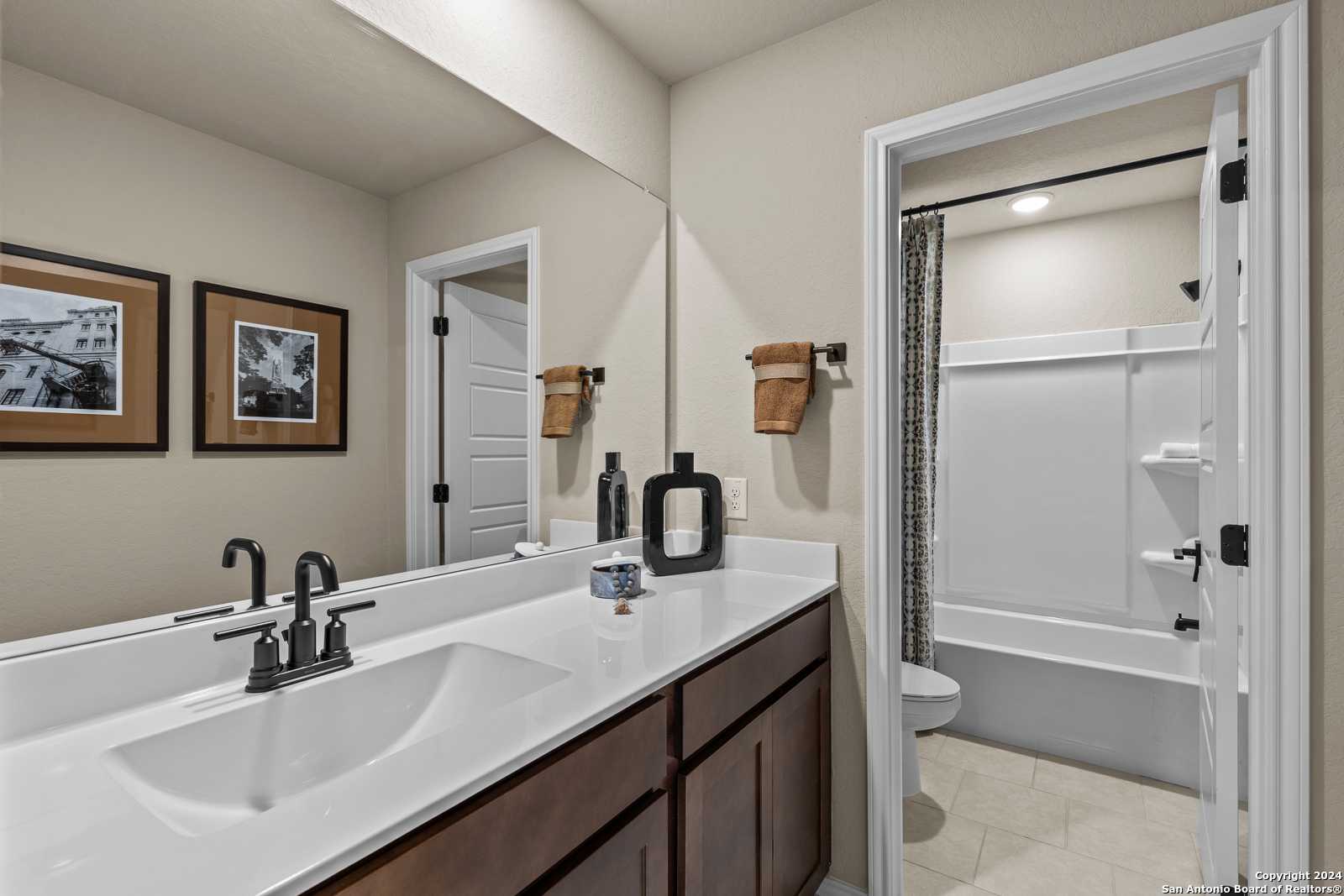 Elegant master bathroom with double vanity, tub-shower combo, and framed art in Davidson Homes The Douglas F, Bricewood, San Antonio