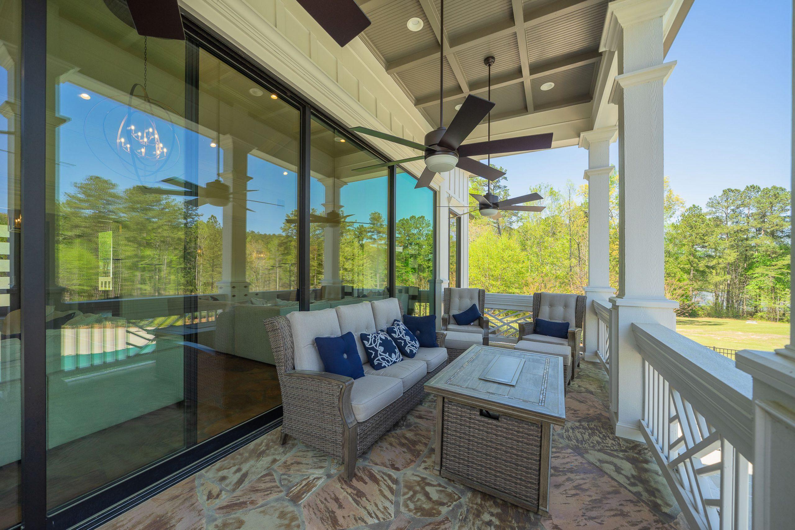 Spacious covered porch at Riverwood in Dallas Georgia with wicker seating, ceiling fans, and sliding doors to modern interior overlooking woods
