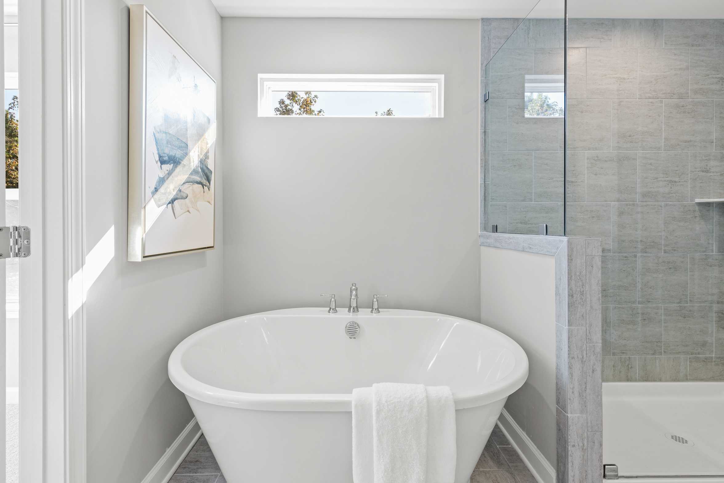 Elegant master bathroom at Prince Place in Fuquay-Varina NC with freestanding clawfoot tub, white towel, and glass shower