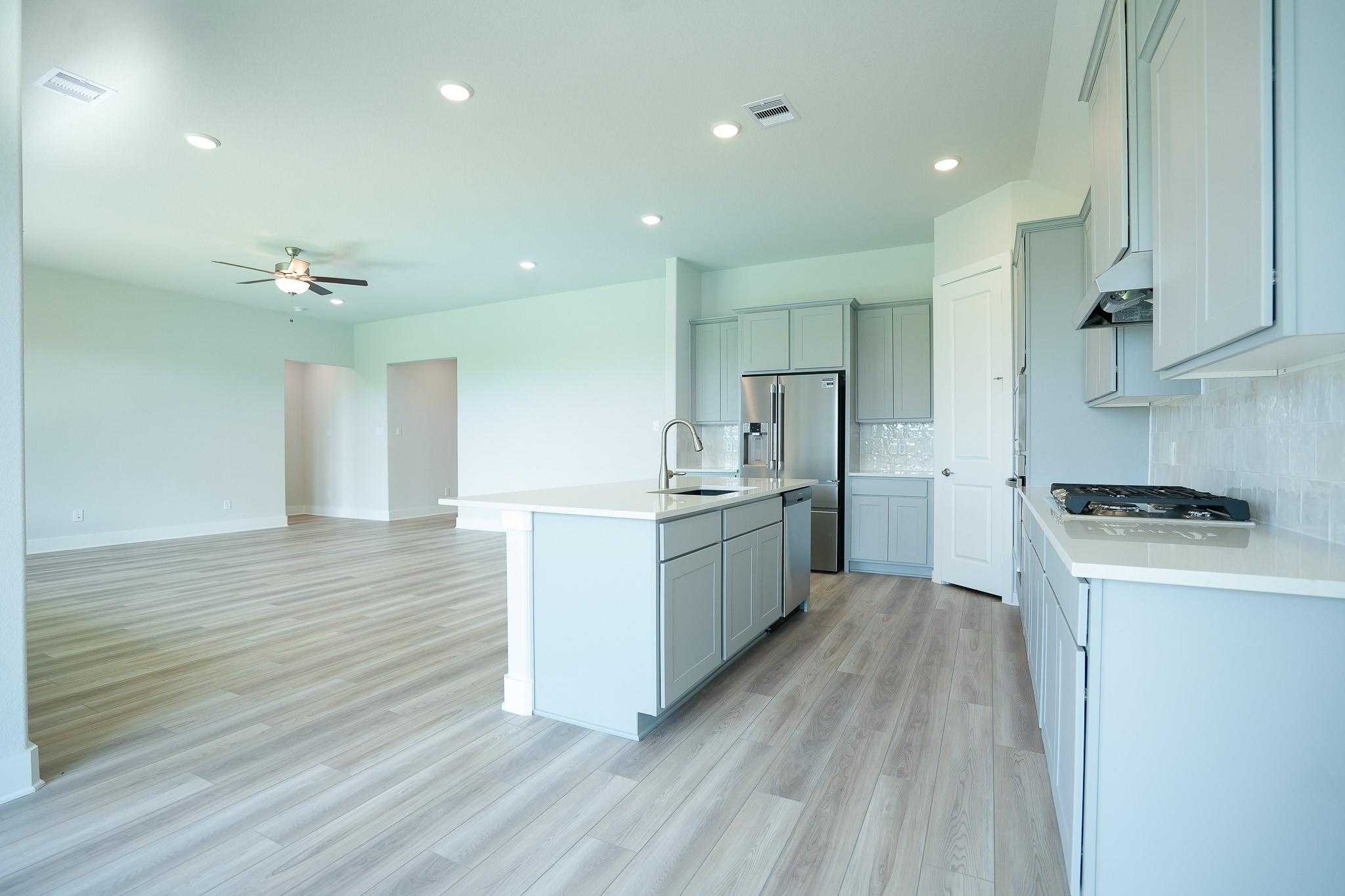 Modern open-concept kitchen with light blue cabinets, stainless steel appliances, quartz island in Davidson Homes The Edward A, Texas City