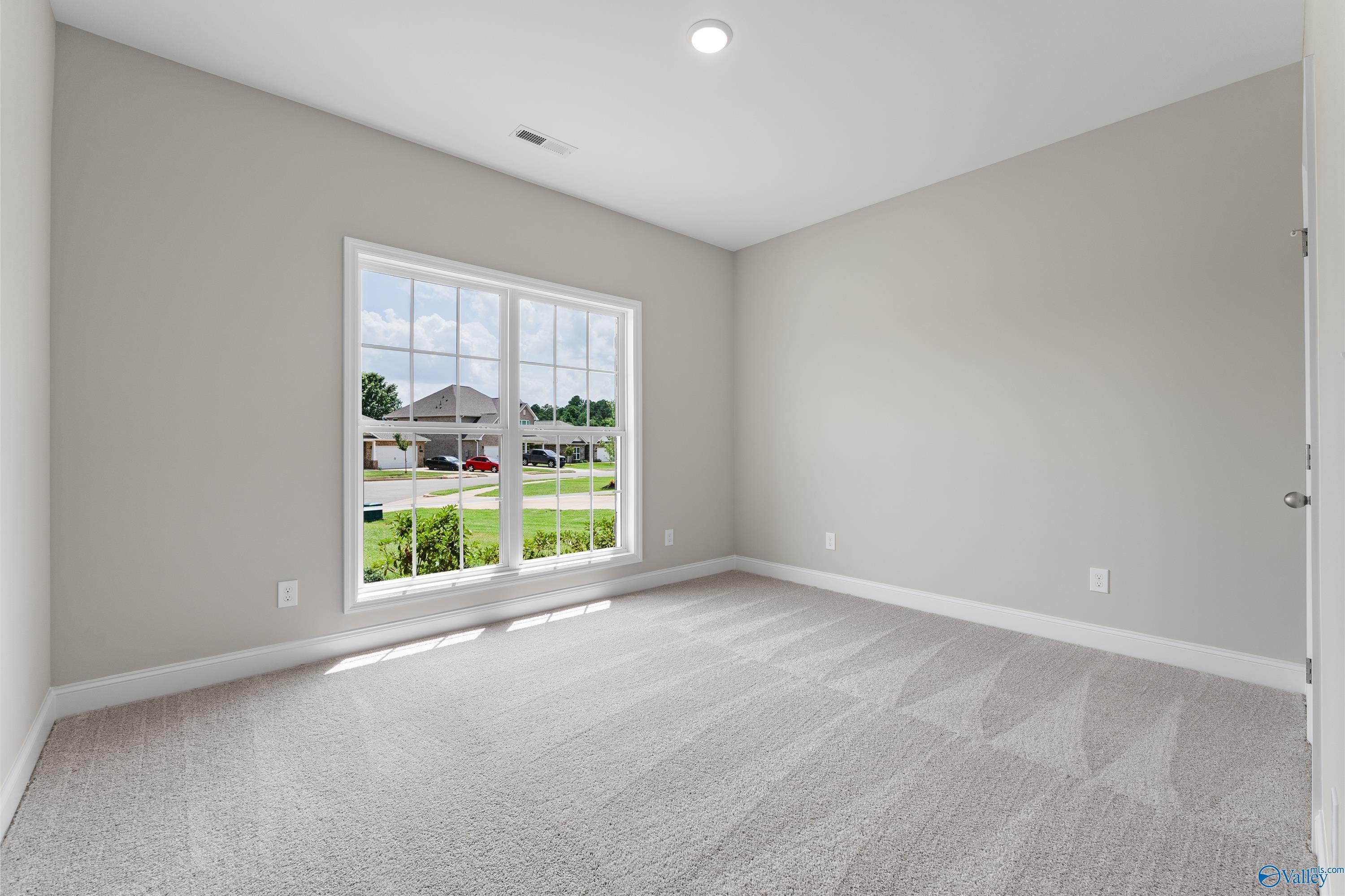 Bright bedroom with gray walls, carpet floor, and large window view in The Daphne C home, Creekside, Harvest, AL