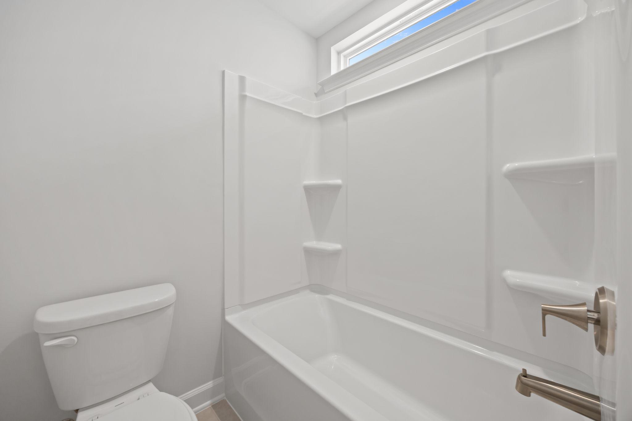 Bright bathroom in The Ashport B featuring a white tub-shower combo with built-in shelving and a transom window.