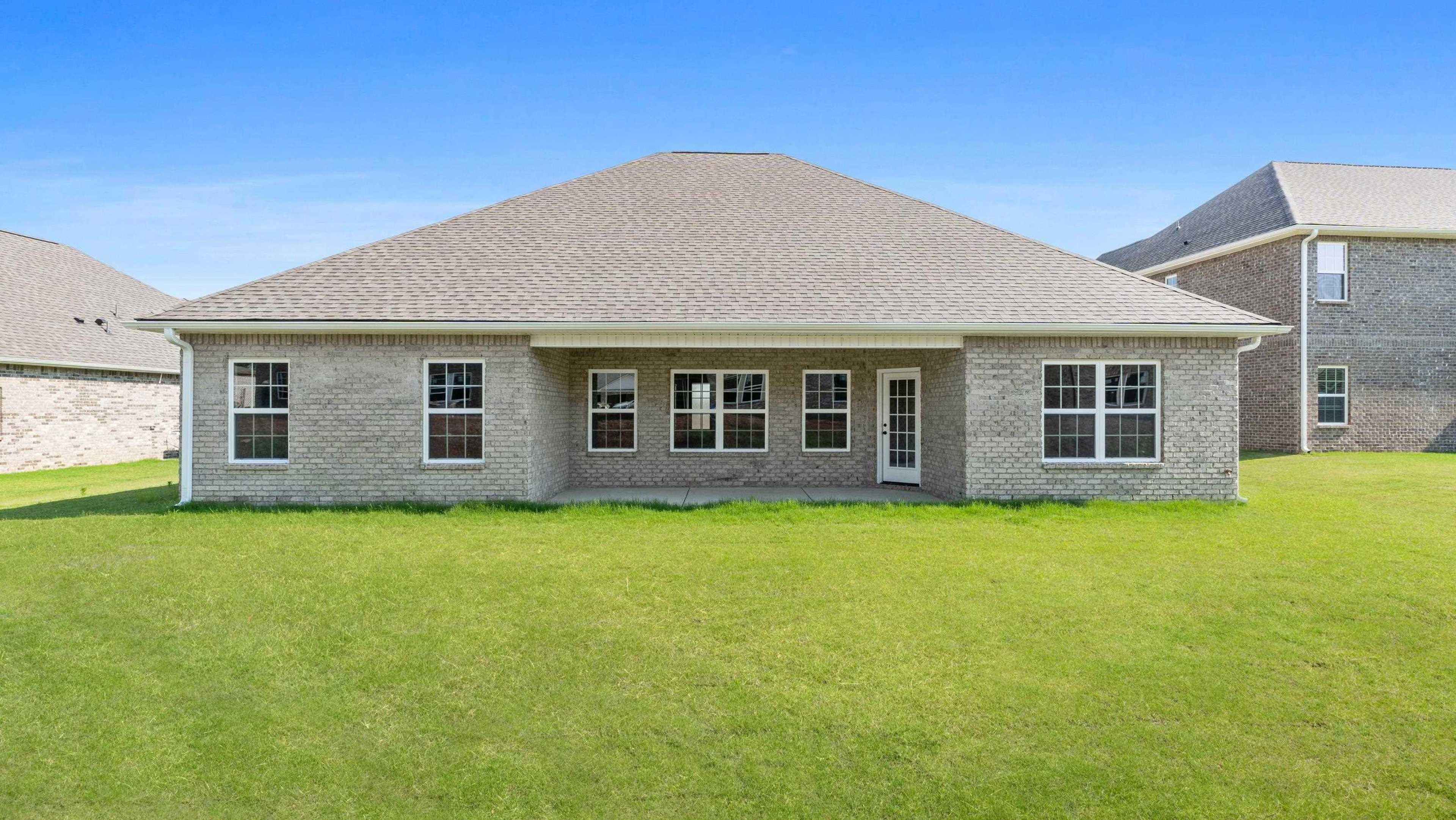 Spacious brick home backyard at Davidson Homes open house, 209 Kendall Farms Boulevard, with sliding doors, large windows, lush green lawn, blue sky