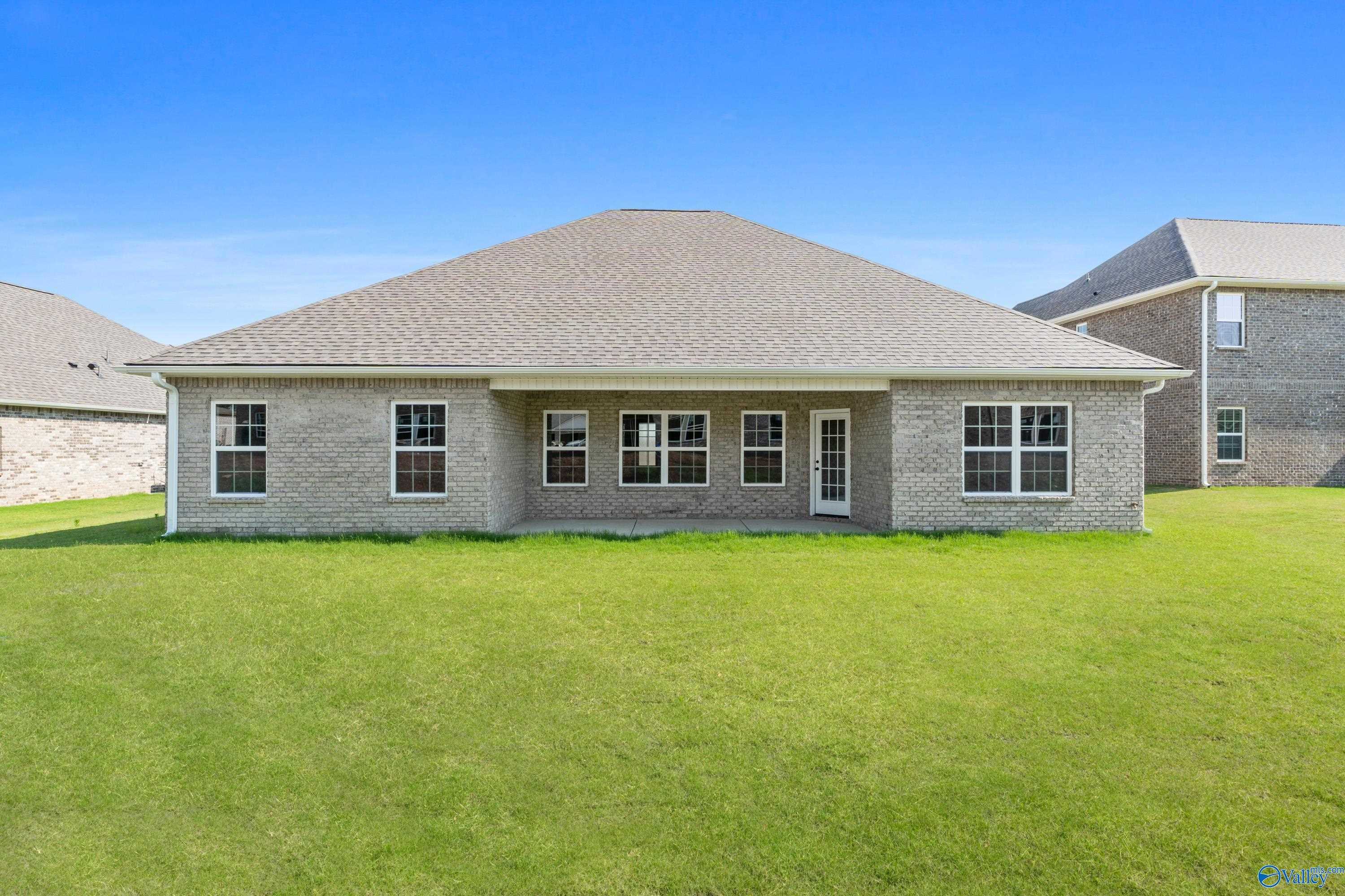 Covered back patio with sliding doors on brick single-story home, lush green yard, blue sky in Kendall Farms, Toney, Alabama