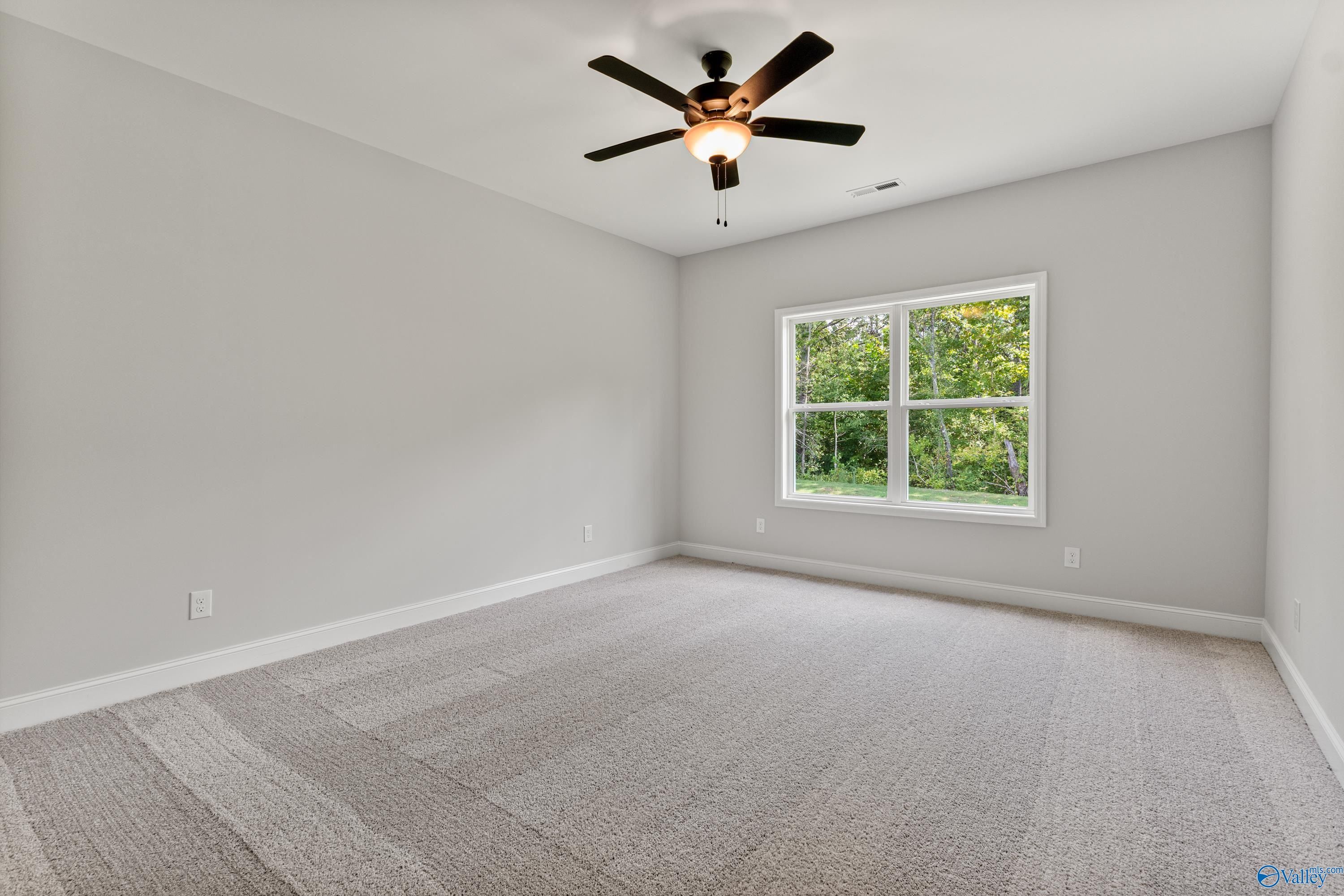 Bright bedroom featuring gray walls, ceiling fan, large window with greenery view, and carpeted floor in Davidson Homes The Daphne, Huntsville