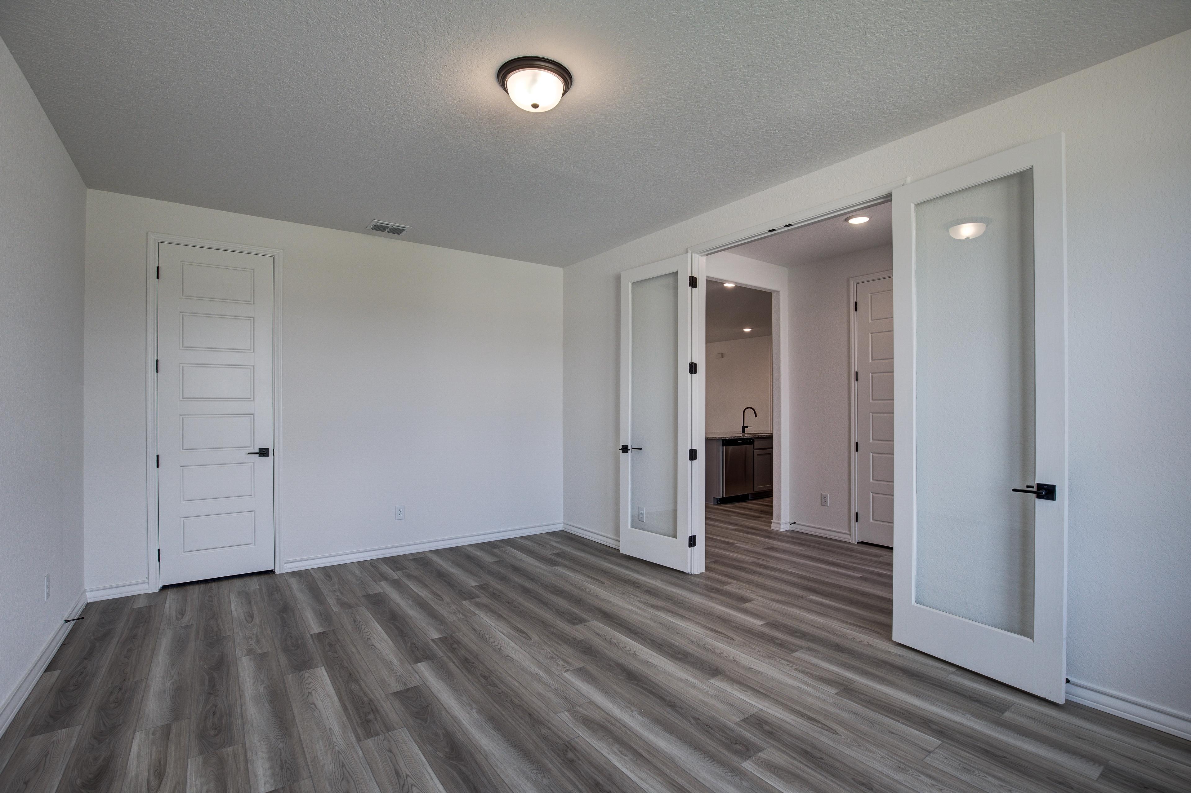 Spacious master suite in The Lanier with luxury vinyl plank floors, white doors, and open glass panels to ensuite bath