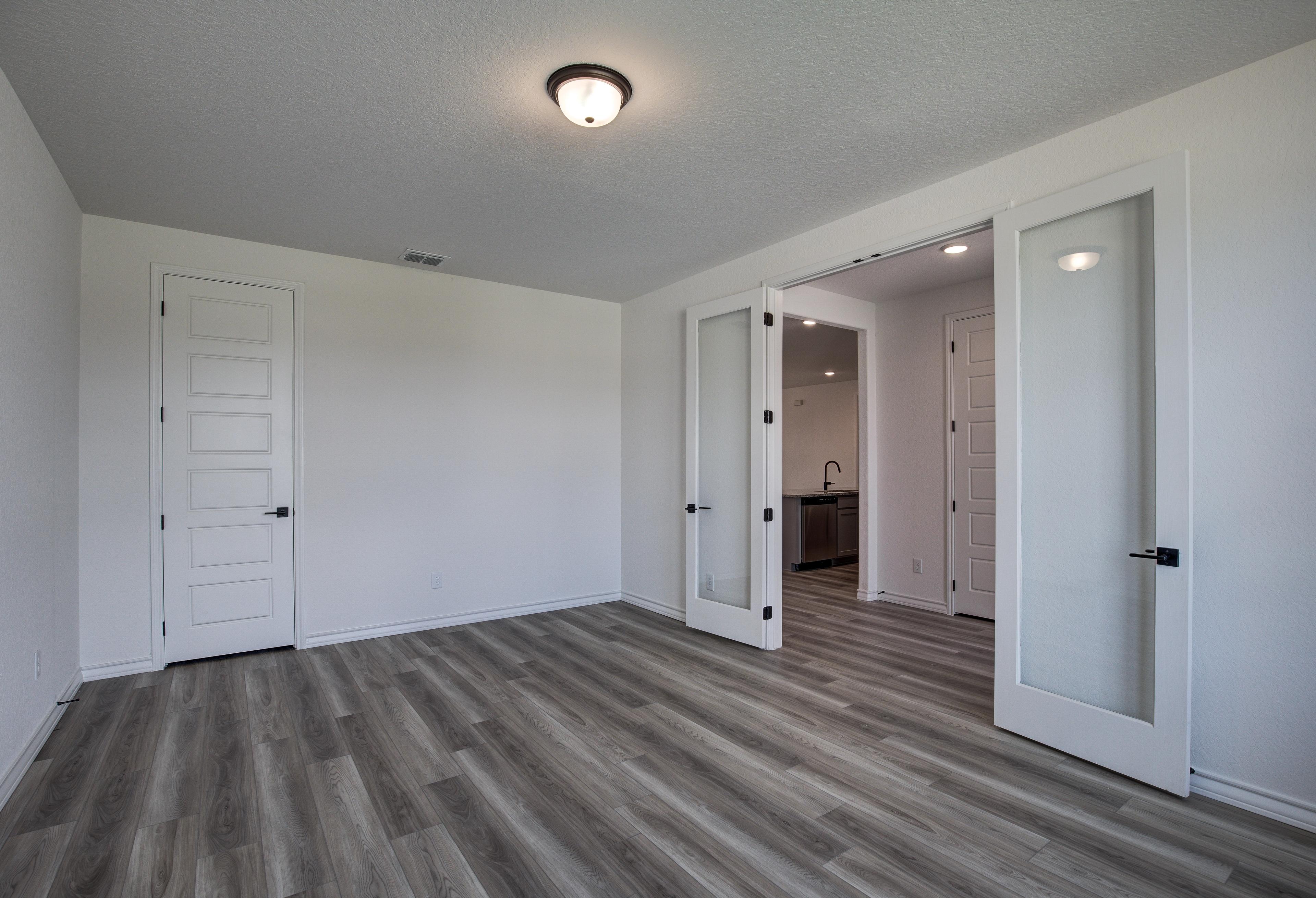 Spacious master suite in The Lanier with luxury vinyl plank floors, white doors, and open glass panels to ensuite bath