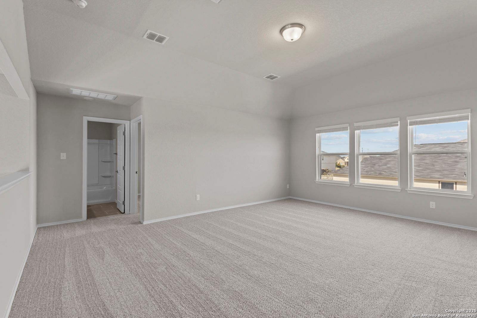 Spacious empty bedroom with gray carpet, light walls, ensuite bath door, and large windows in Davidson Homes The Collin B, Seguin, Texas