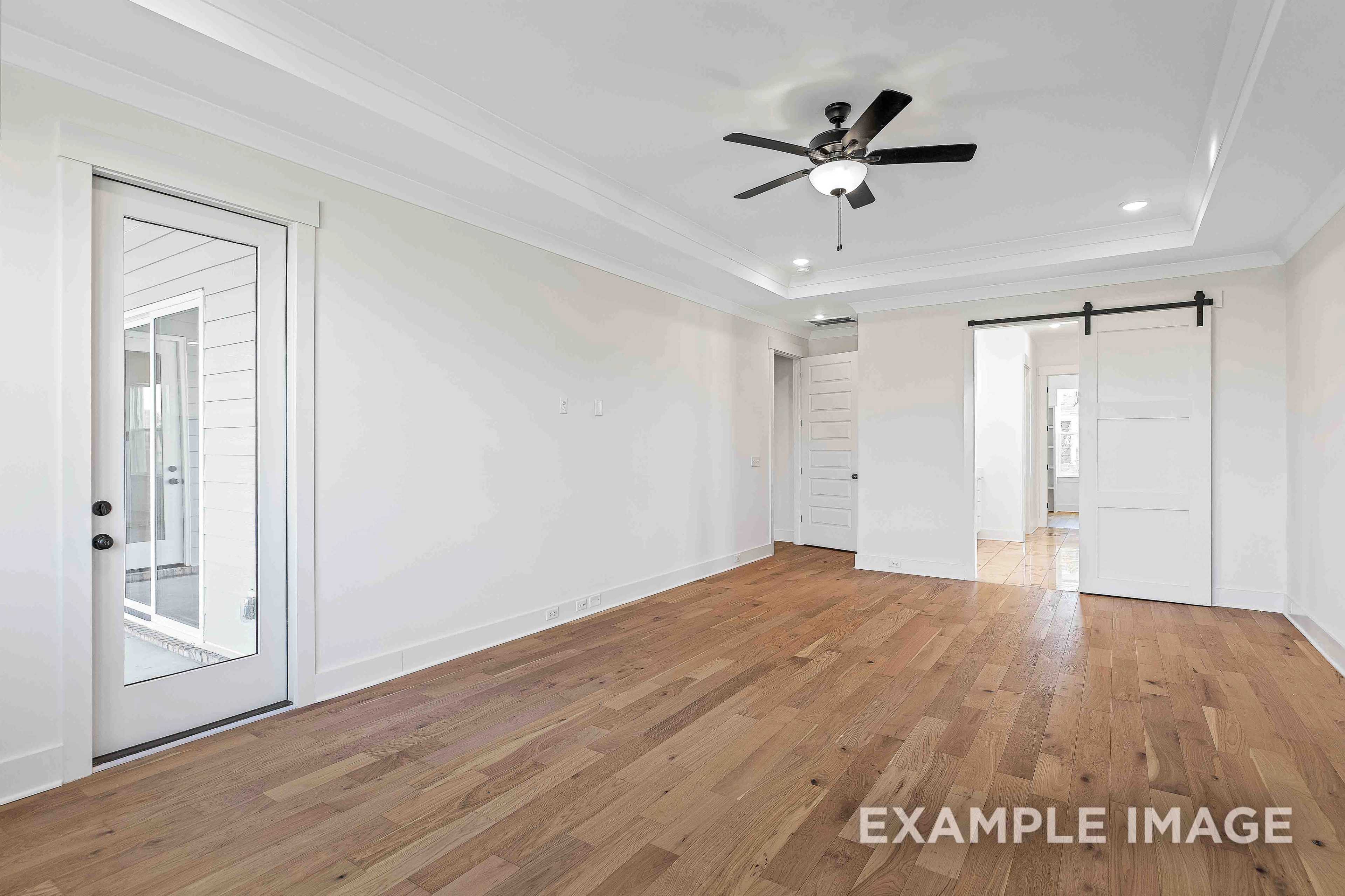 Spacious master bedroom in The Albany A with hardwood floors, ceiling fan, and open barn door to ensuite