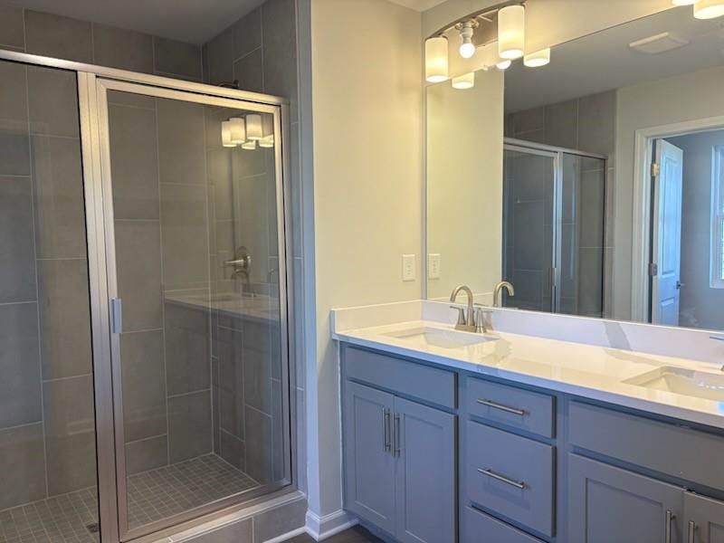 Modern master bathroom with glass shower enclosure, double vanity, and gray cabinets in Davidson Homes Marion A, Winder GA