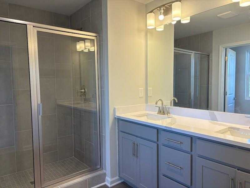 Modern master bathroom with glass shower enclosure, double vanity, and gray cabinets in Davidson Homes Marion A, Winder GA