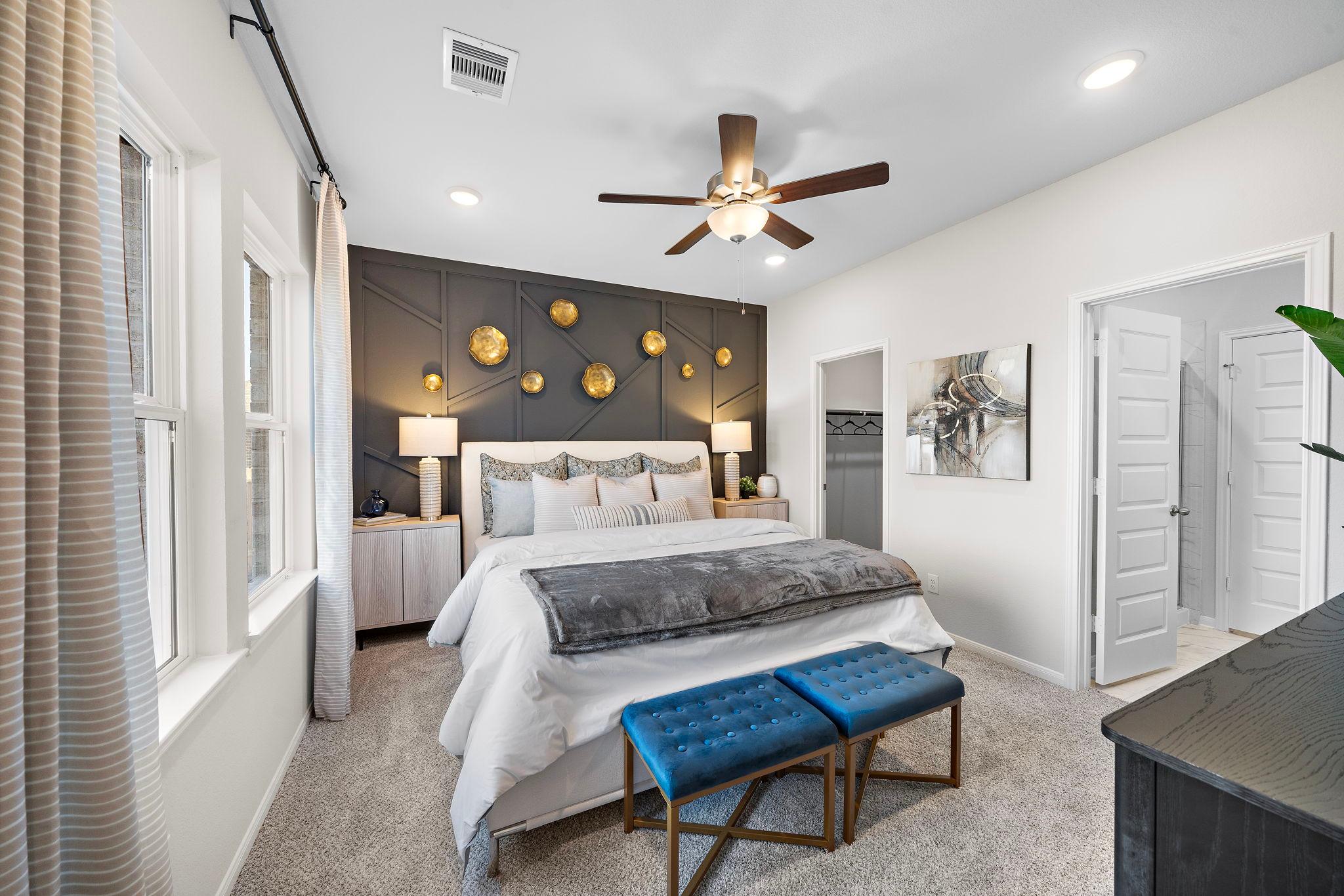 Spacious master bedroom at Lakes at Black Oak in Magnolia Texas with king bed, gold accent wall, ceiling fan, and blue bench