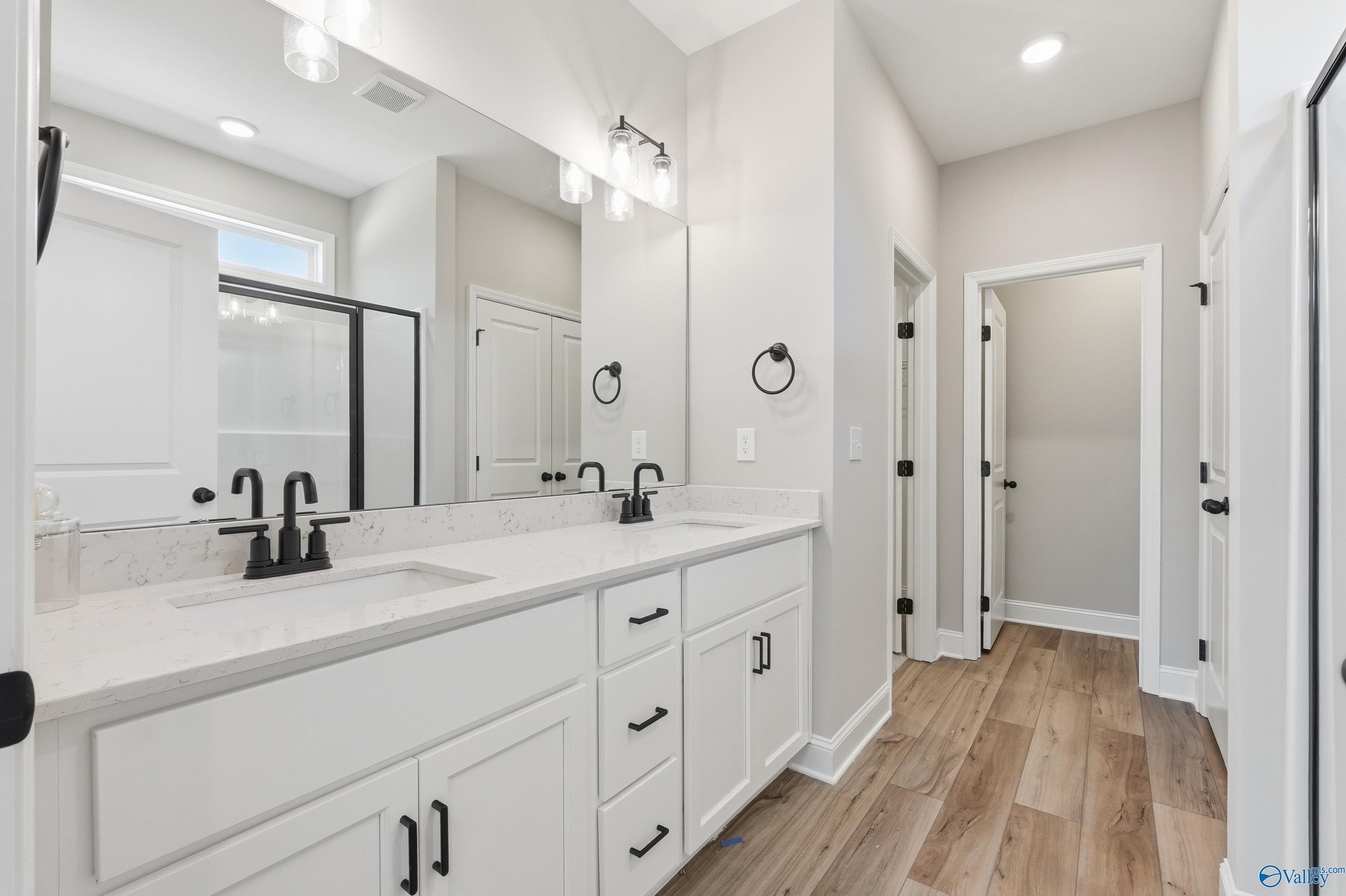Modern master bathroom featuring double white vanity, quartz countertop, black faucets, and glass shower in Davidson Homes The Laurel K, Cullman AL