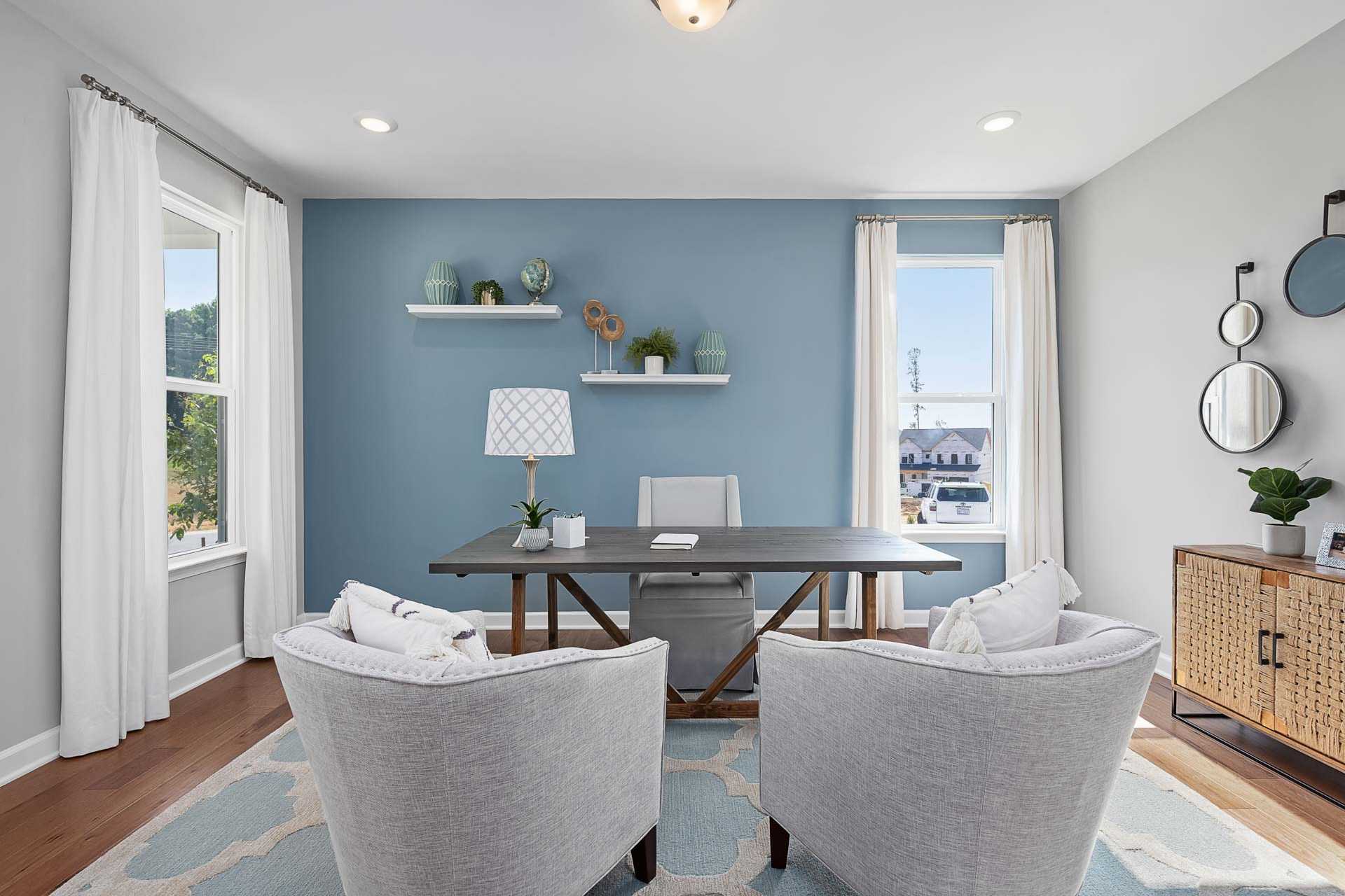 Modern home office at Highland Forest in Fuquay-Varina, NC with blue walls, wooden desk, armchairs, plants, and large windows