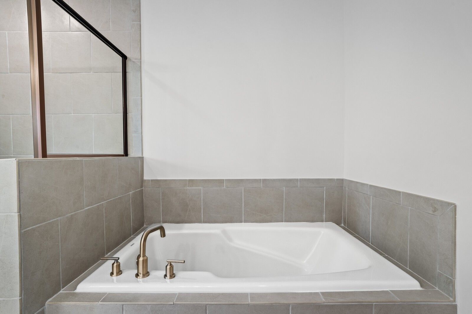 Deep soaking tub with tile surround and bronze fixtures in master bathroom of The Logan C home in Calista Farms.