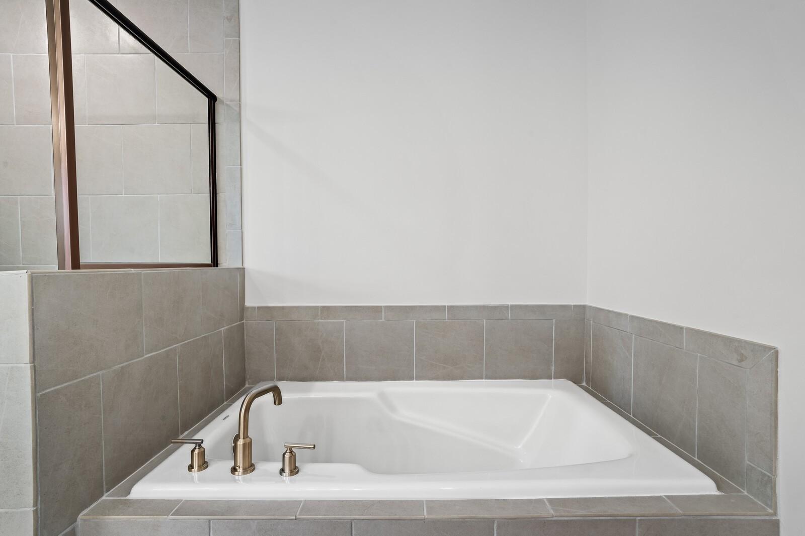 Deep soaking tub with tile surround and bronze fixtures in master bathroom of The Logan C home in Calista Farms.