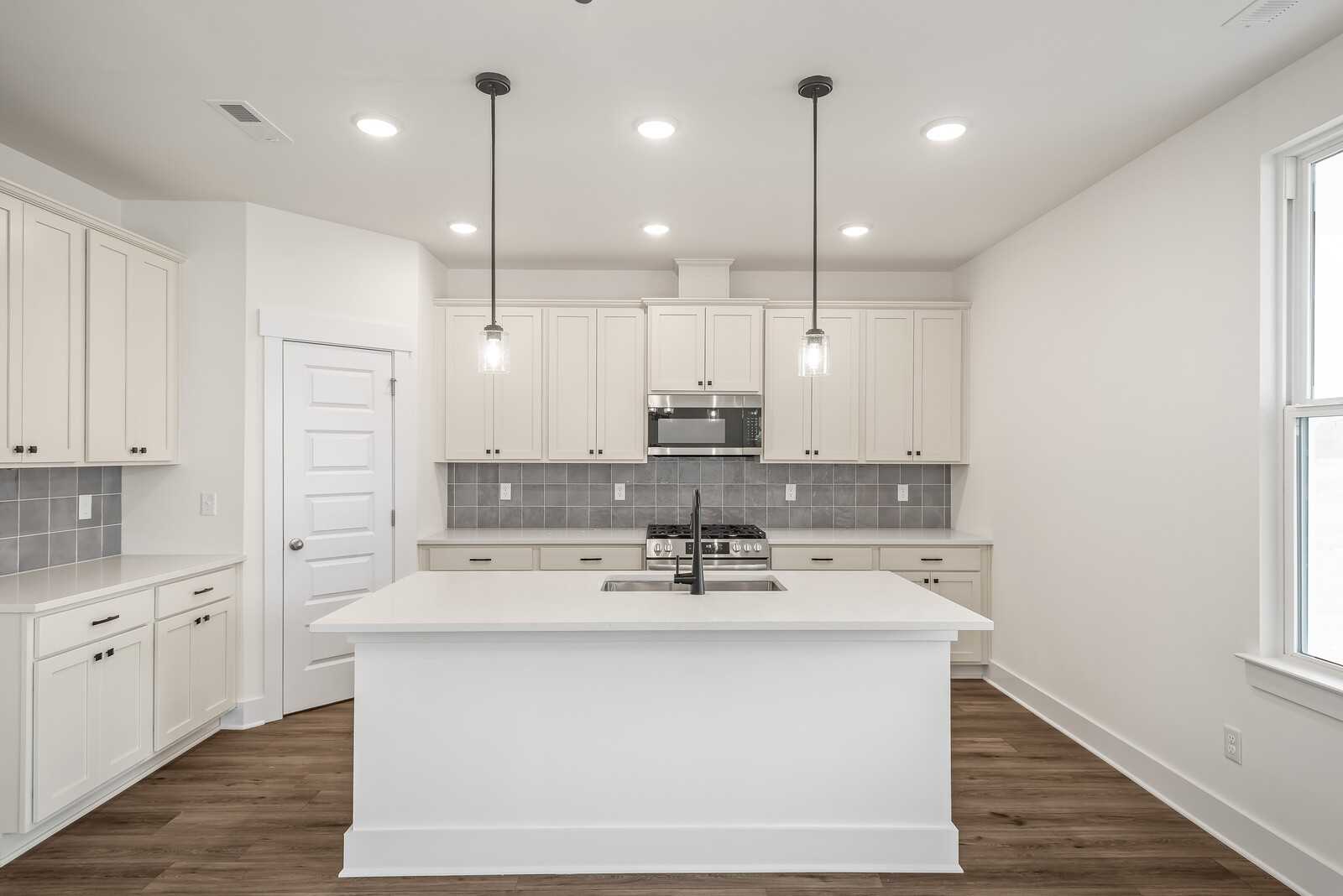 Modern white kitchen with large island, stainless steel appliances, subway tile backsplash in The Logan C by Davidson Homes, Gallatin, TN