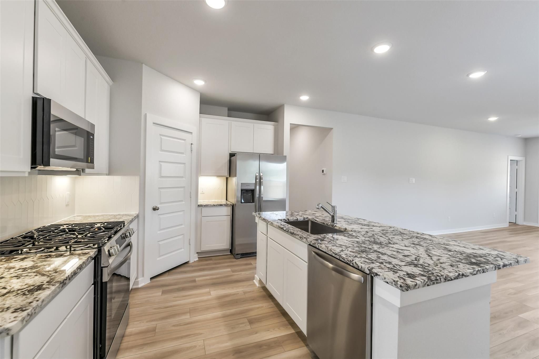 Open-concept kitchen with white cabinets, speckled granite island, stainless steel gas range and appliances in San Marcos E, Conroe TX
