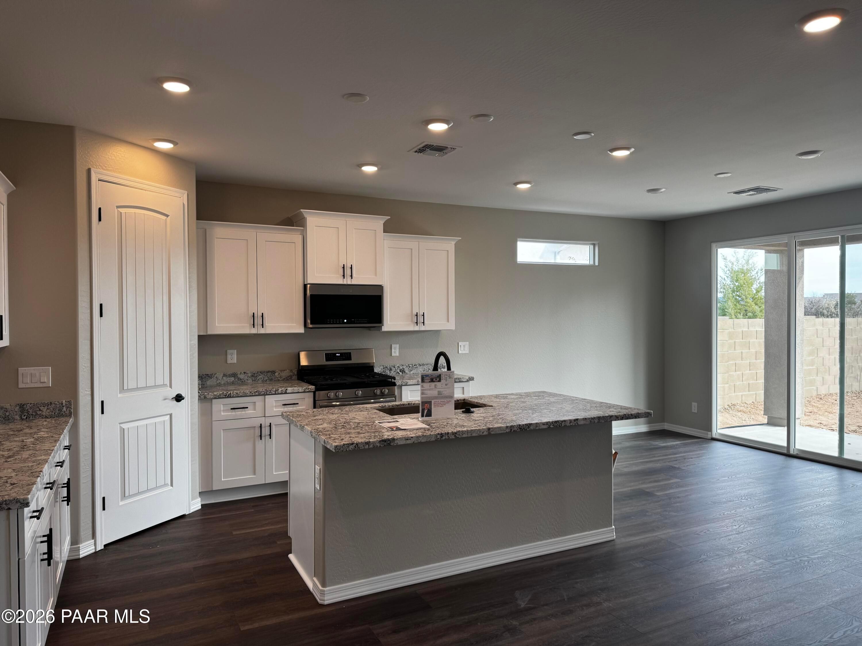 Modern kitchen with white shaker cabinets, granite island, stainless appliances, and sliding doors to backyard in Durango II B, Prescott AZ