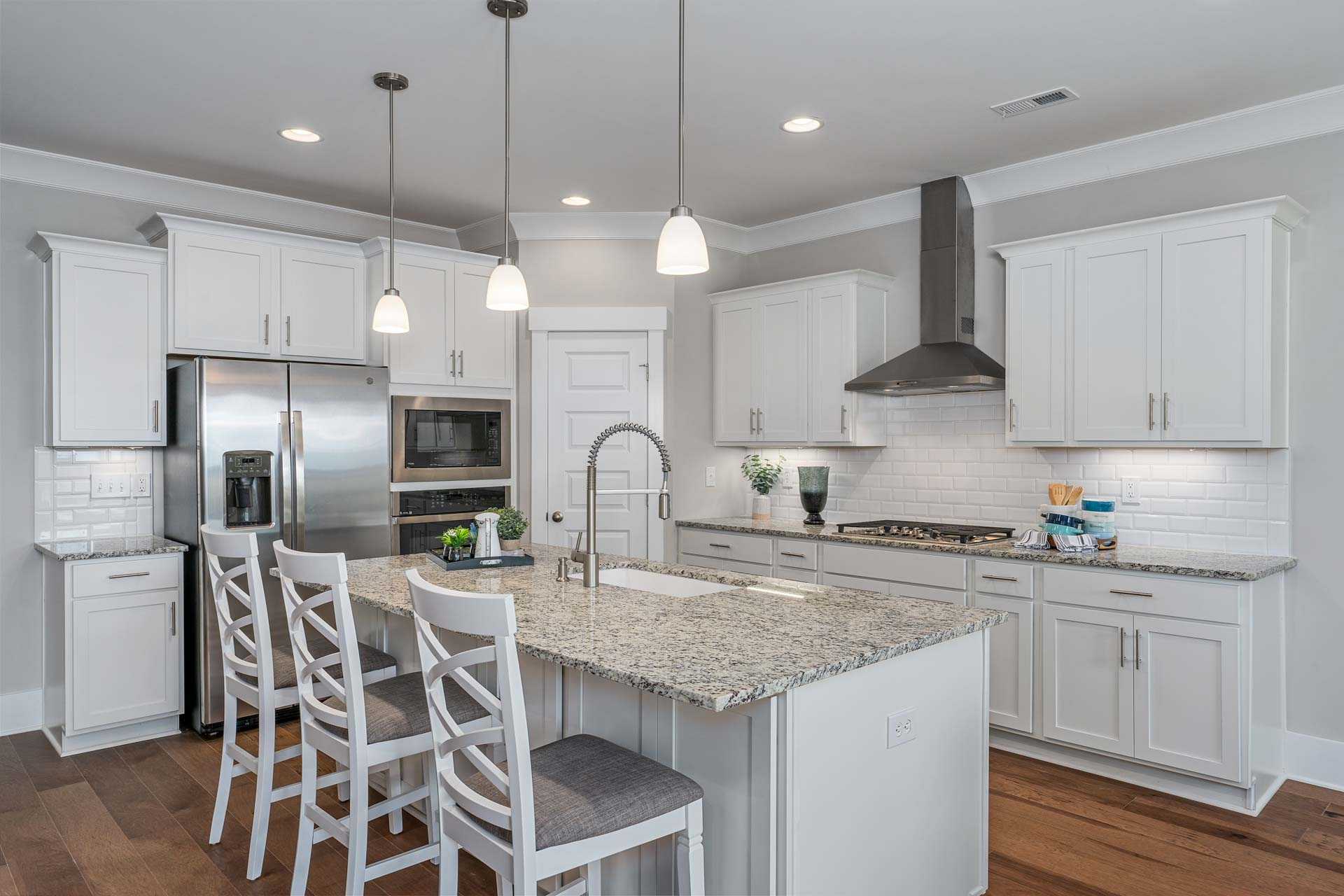 Spacious white kitchen in Kendall Downs Toney Alabama with granite island bar stools subway tile backsplash and hardwood floors