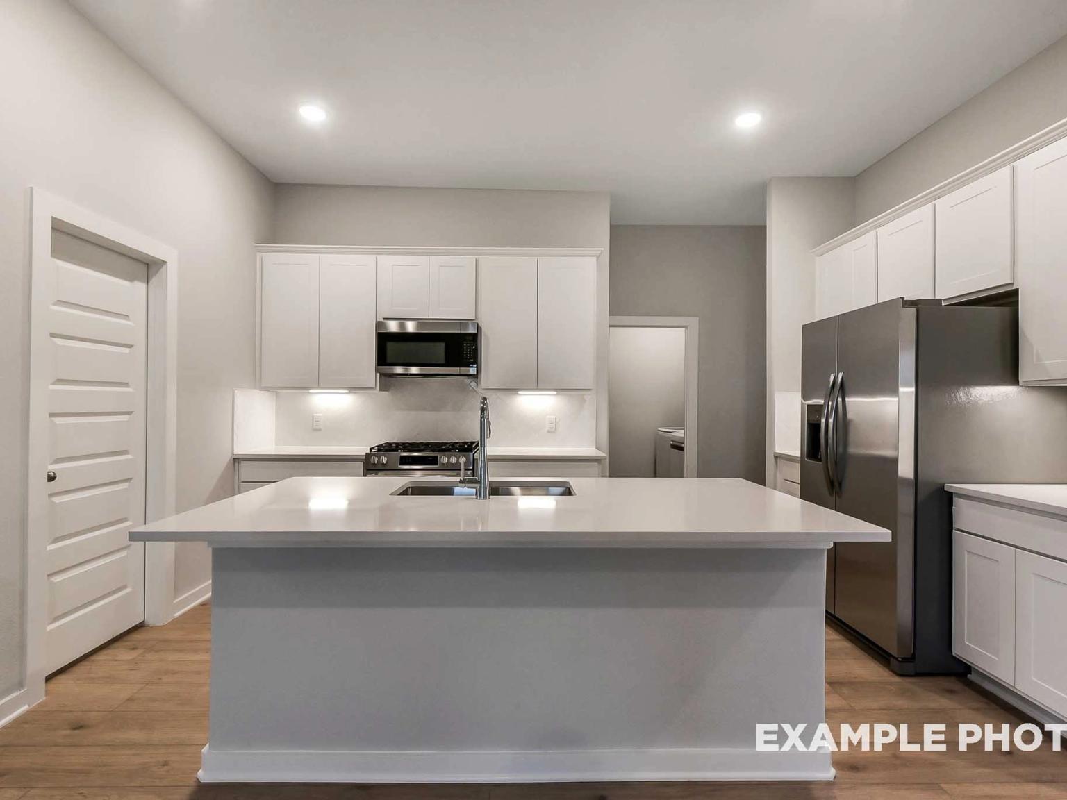 Modern kitchen with white cabinets, quartz island, and stainless appliances in The Brookside F, Enclave at Newport, Crosby.