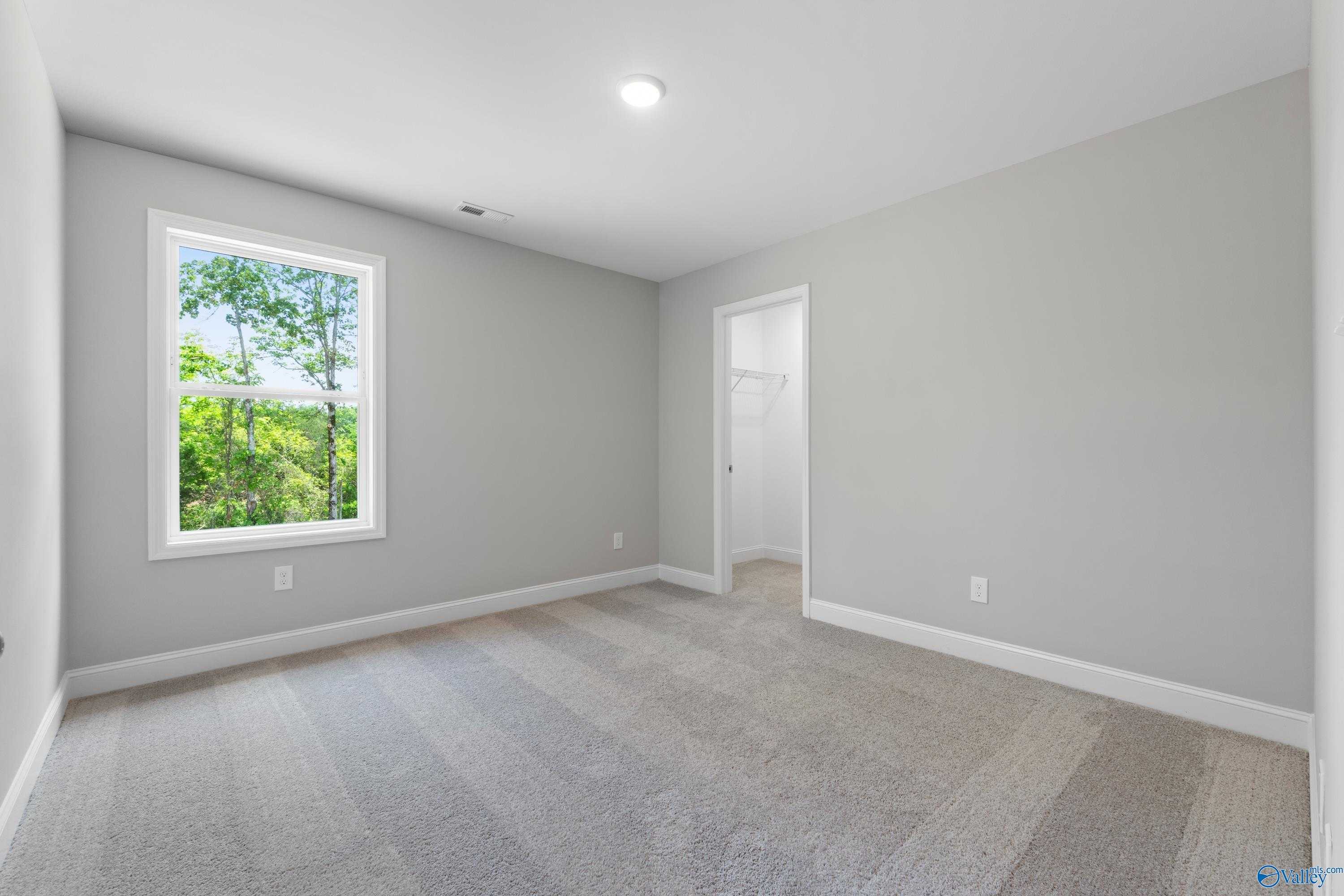 Bright secondary bedroom with gray walls, large window overlooking wooded greenery, carpeted floor in Davidson Homes Chelsea B, New Market AL