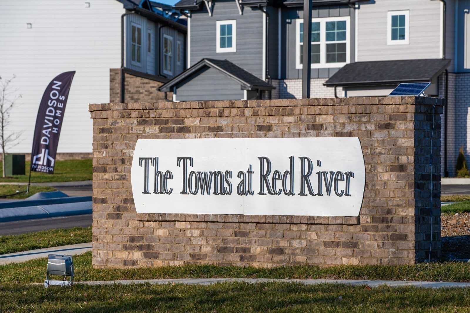 Brick entrance sign for The Towns at Red River by Davidson Homes in Gallatin, Tennessee, with townhomes and flags