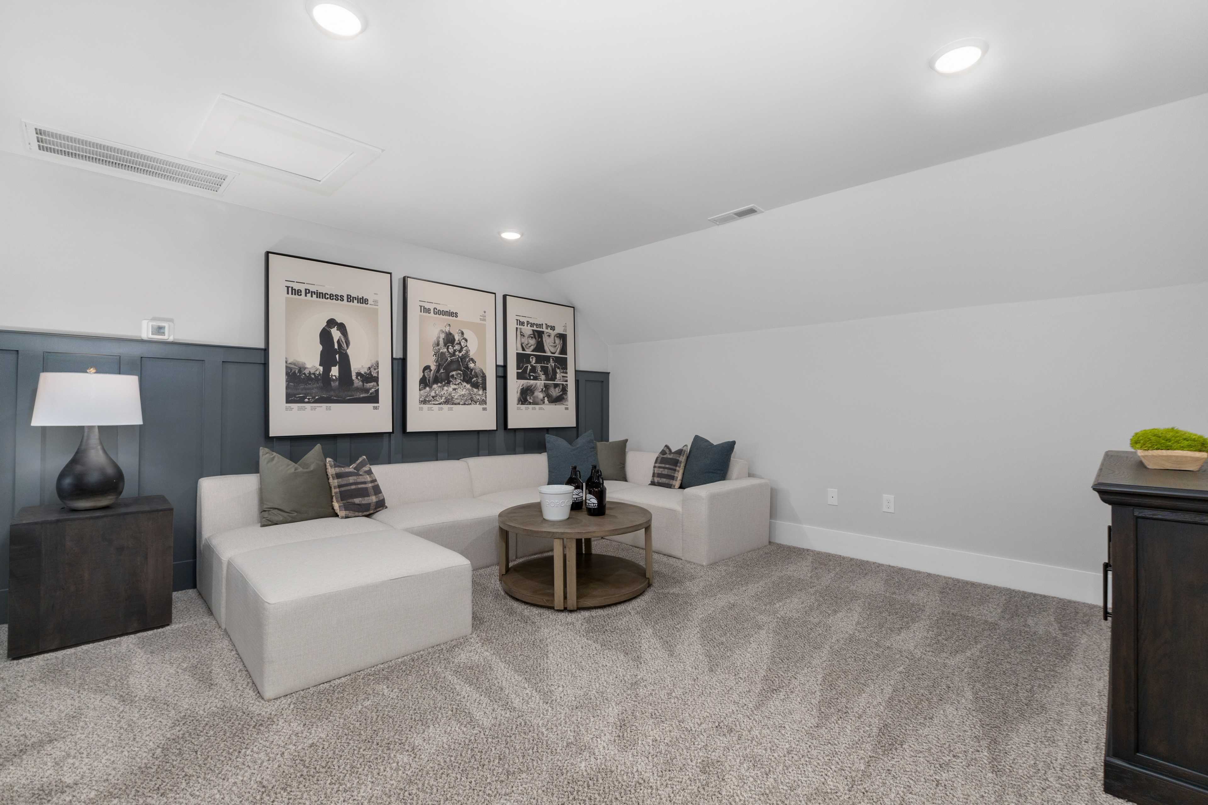 Cozy bonus room at Kendall Farms in Toney Alabama with white sectional sofa, shiplap wall, framed artwork, and carpeted floor