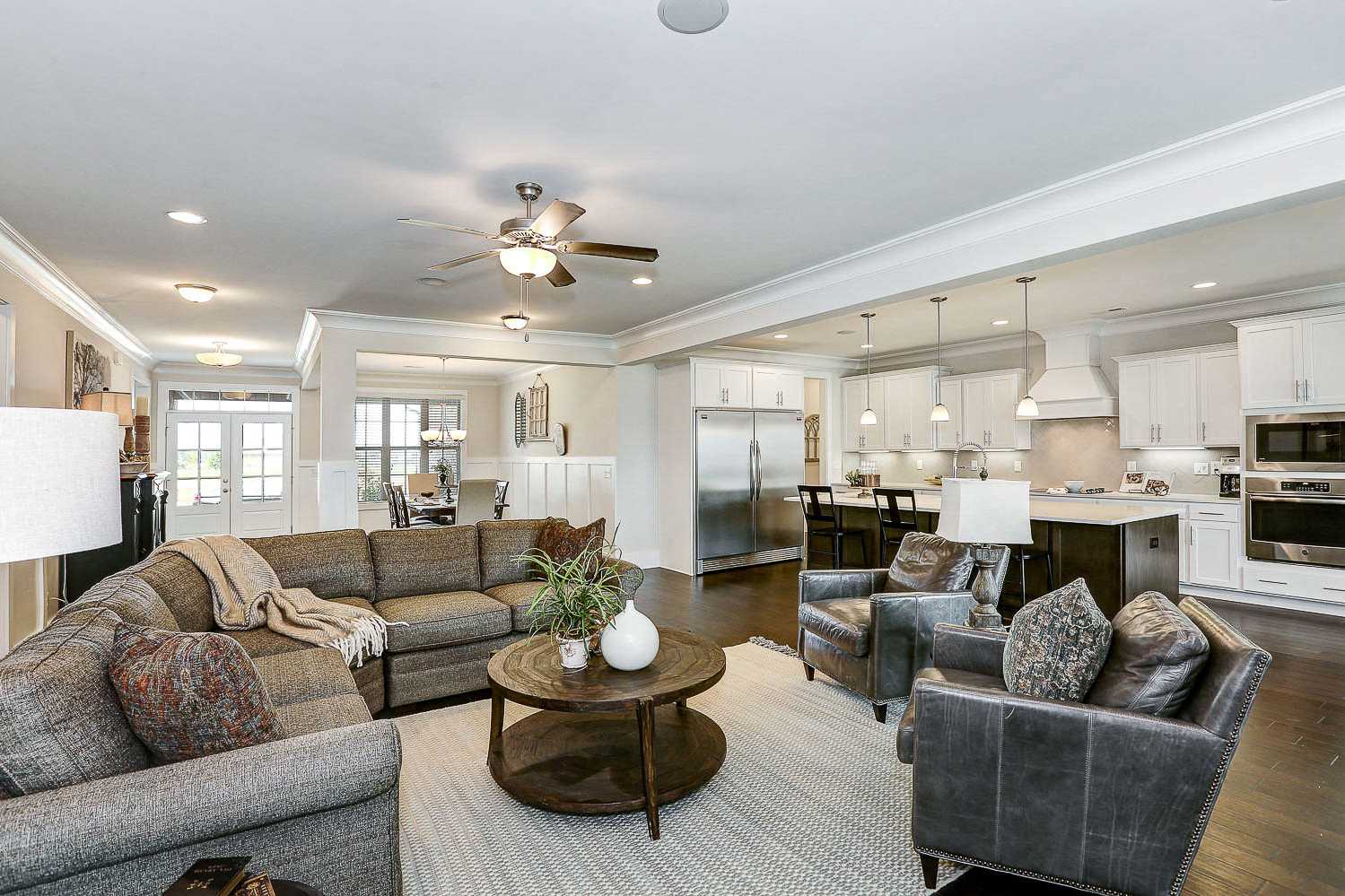 Open-concept living room and kitchen in The Finleigh by Davidson Homes, with sectional sofa, leather chairs, white cabinets, and island